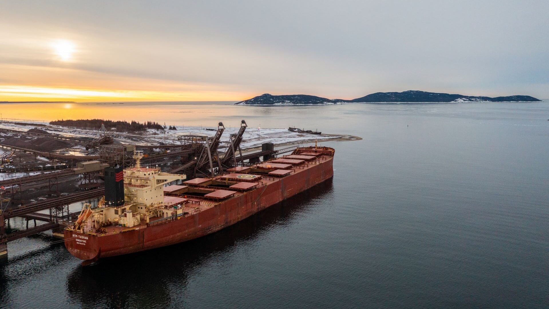 Bulk carrier vessel loading at port, with sunset behind