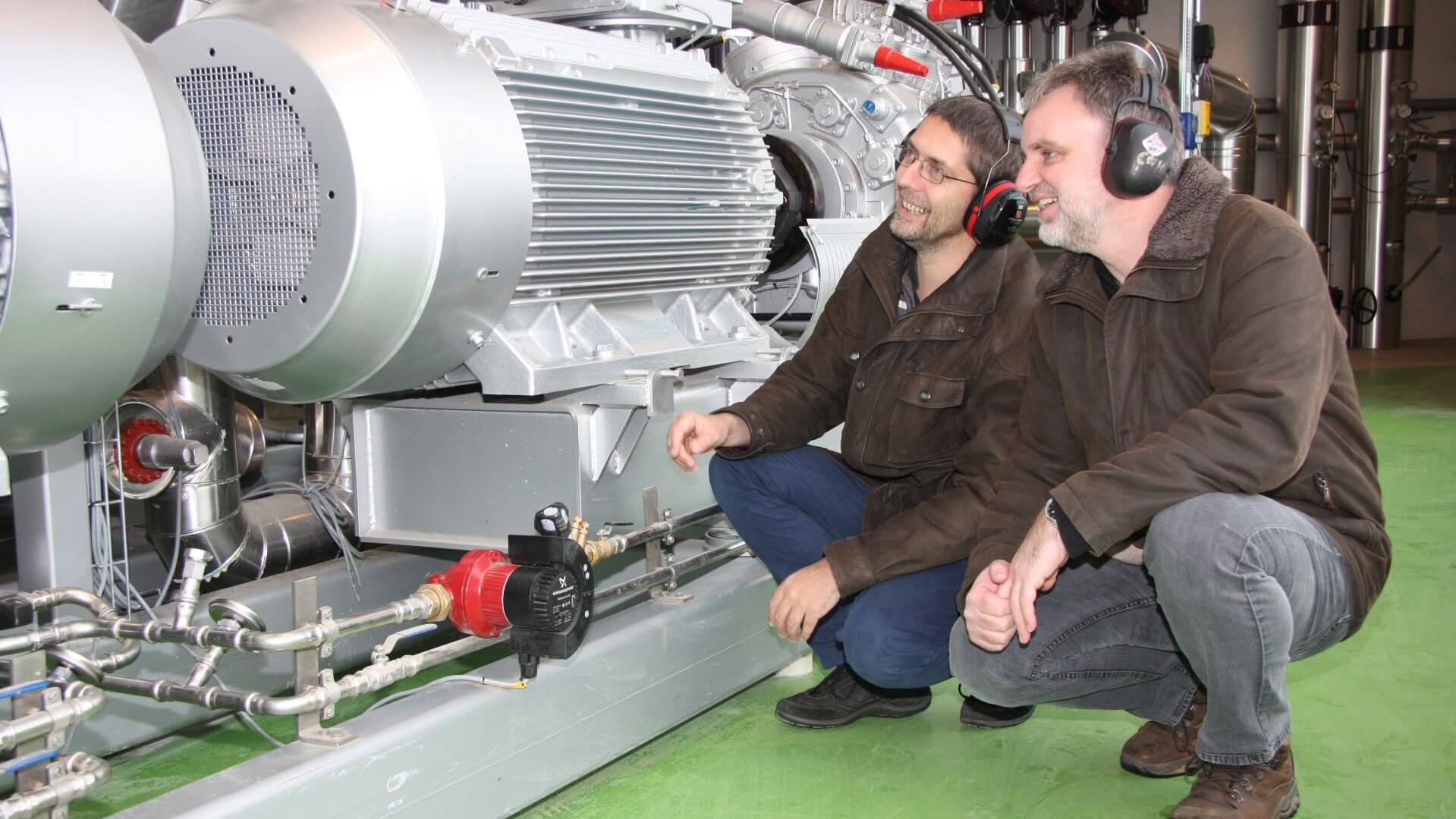 Two men crouched down next to and studying a heat pump