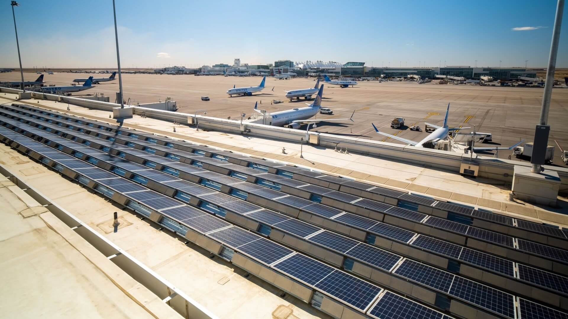 Aerial view over Denver International Airport's solar farm panels with planes in the background