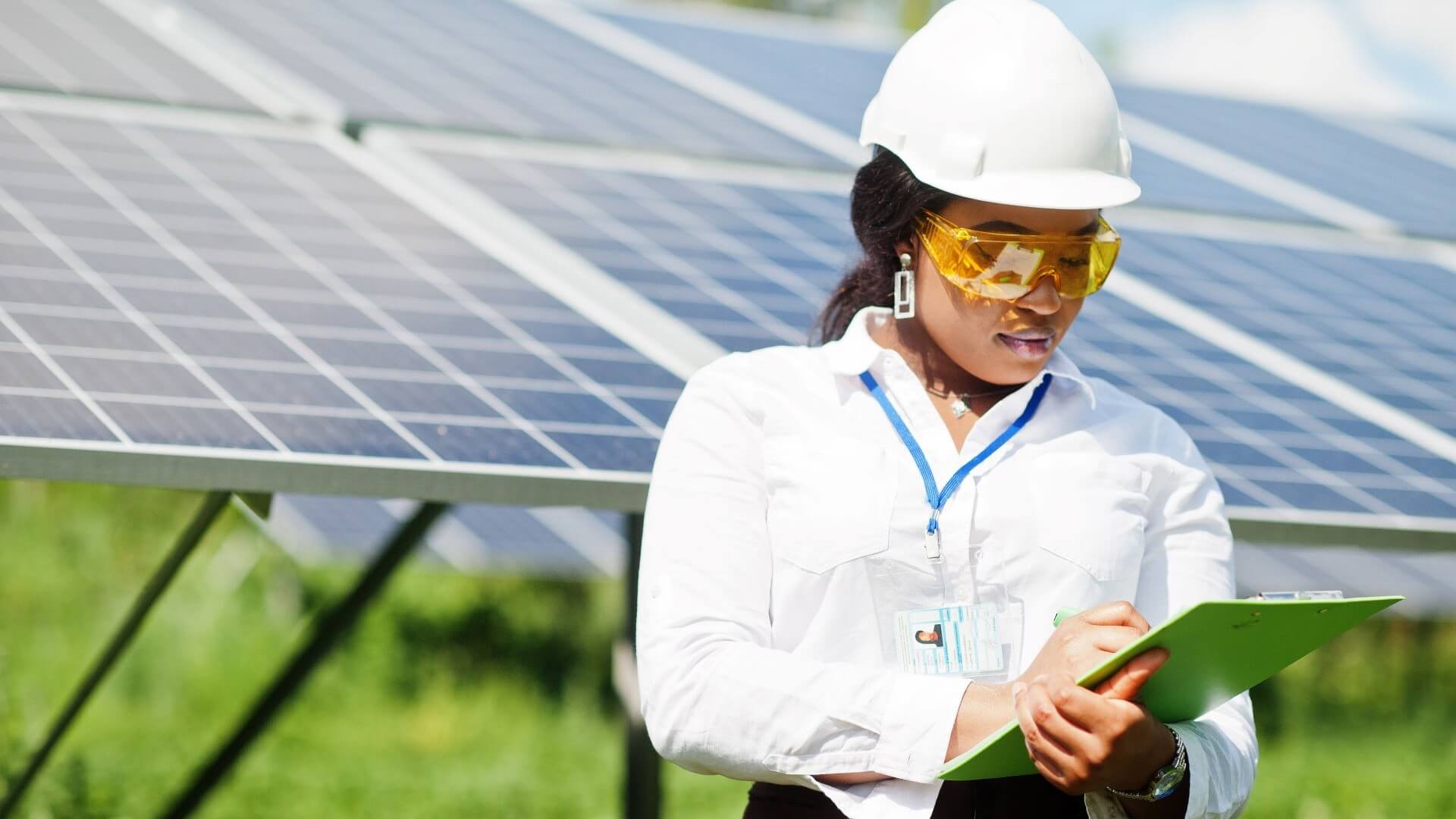 Woman engineer in white boiler suit and hard hard in front of solar panels