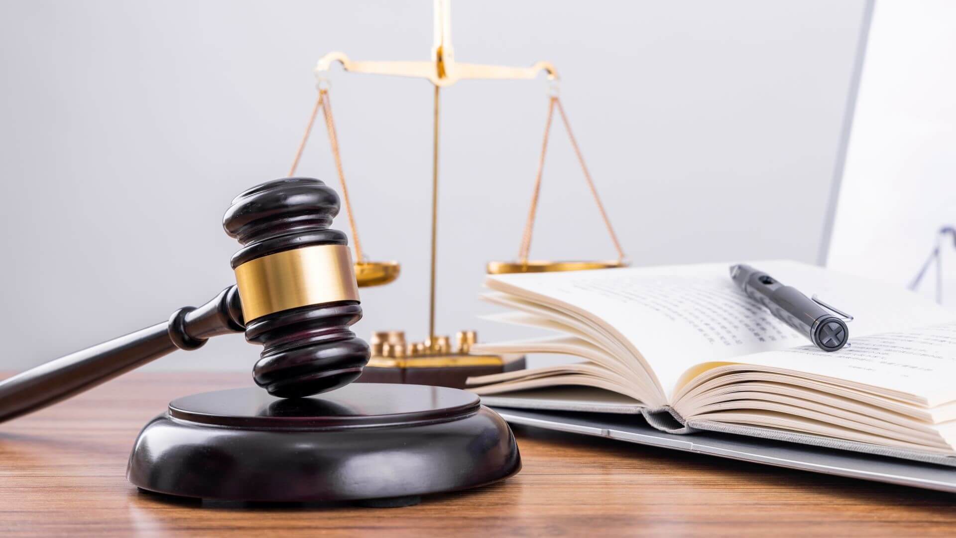 Close up of judge's gavel, scales of justice and open legal book with pen resting on pages