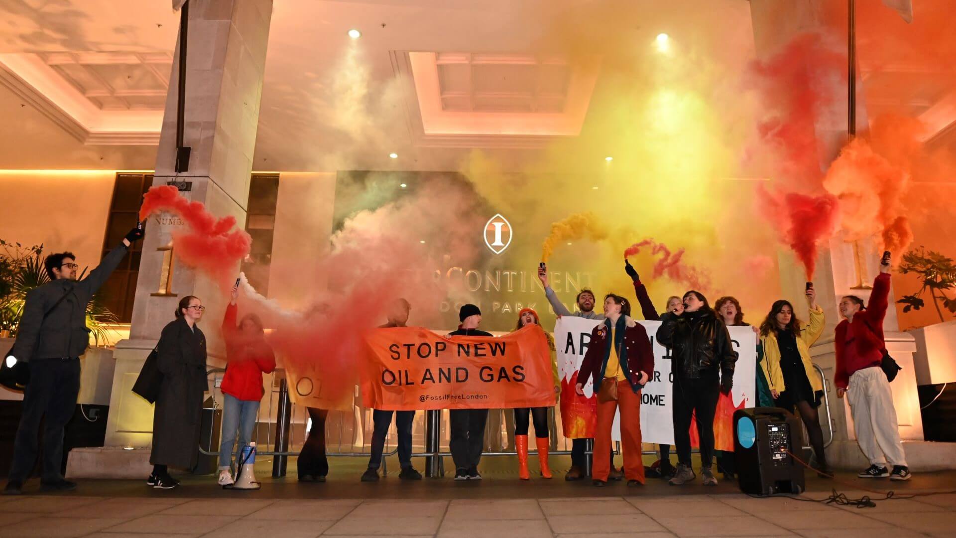 Group of Fossil Free London activists protesting with banners and smoke bombs outside International Energy Week 2023 venue