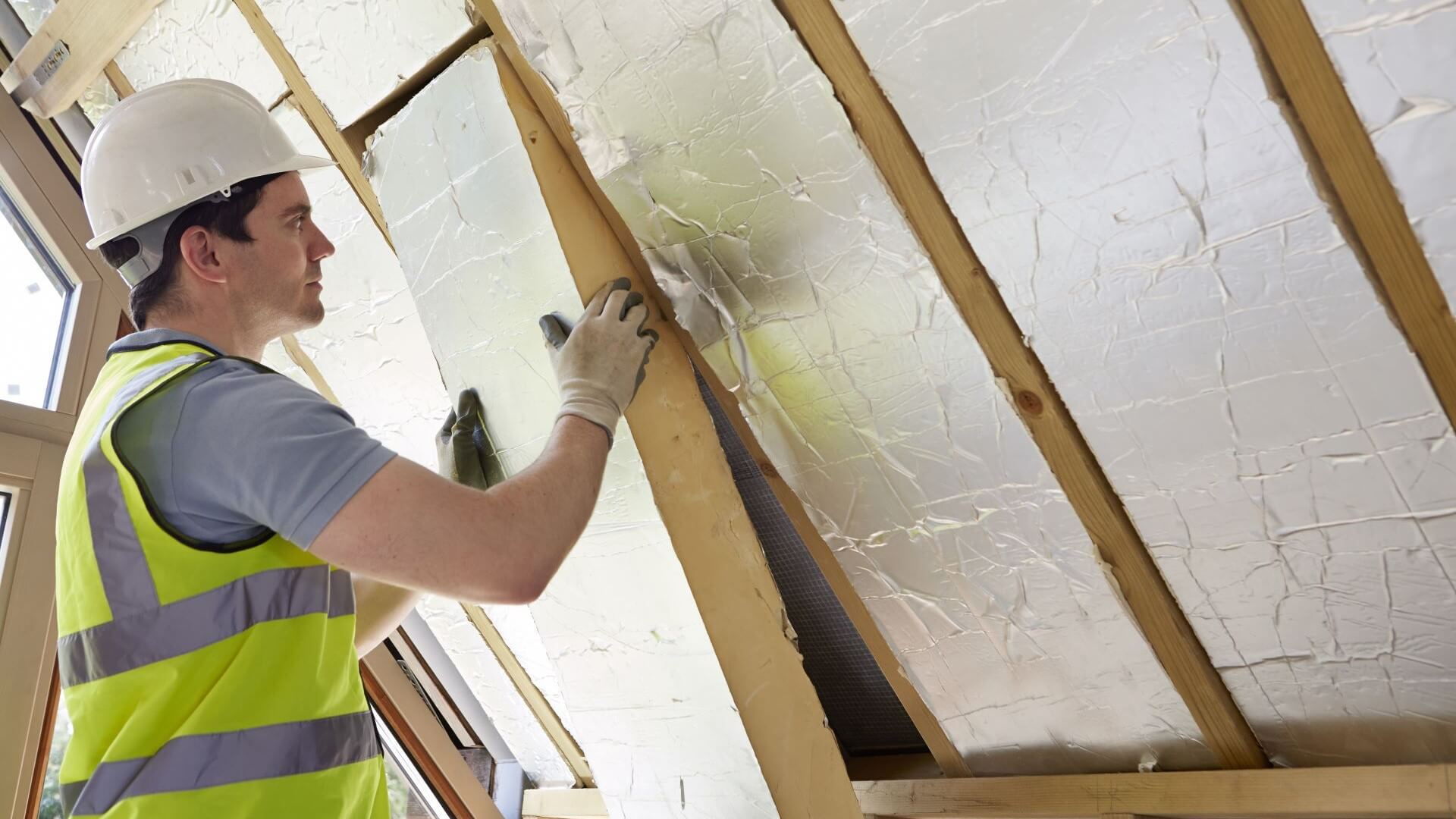 Man in high-viz jacket and hard hat installing roofing insulation in house