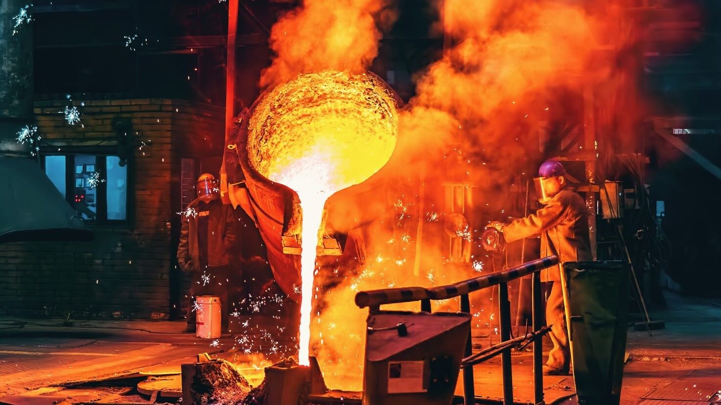 Man pouring liquid hot metal from a large cauldron in a factory