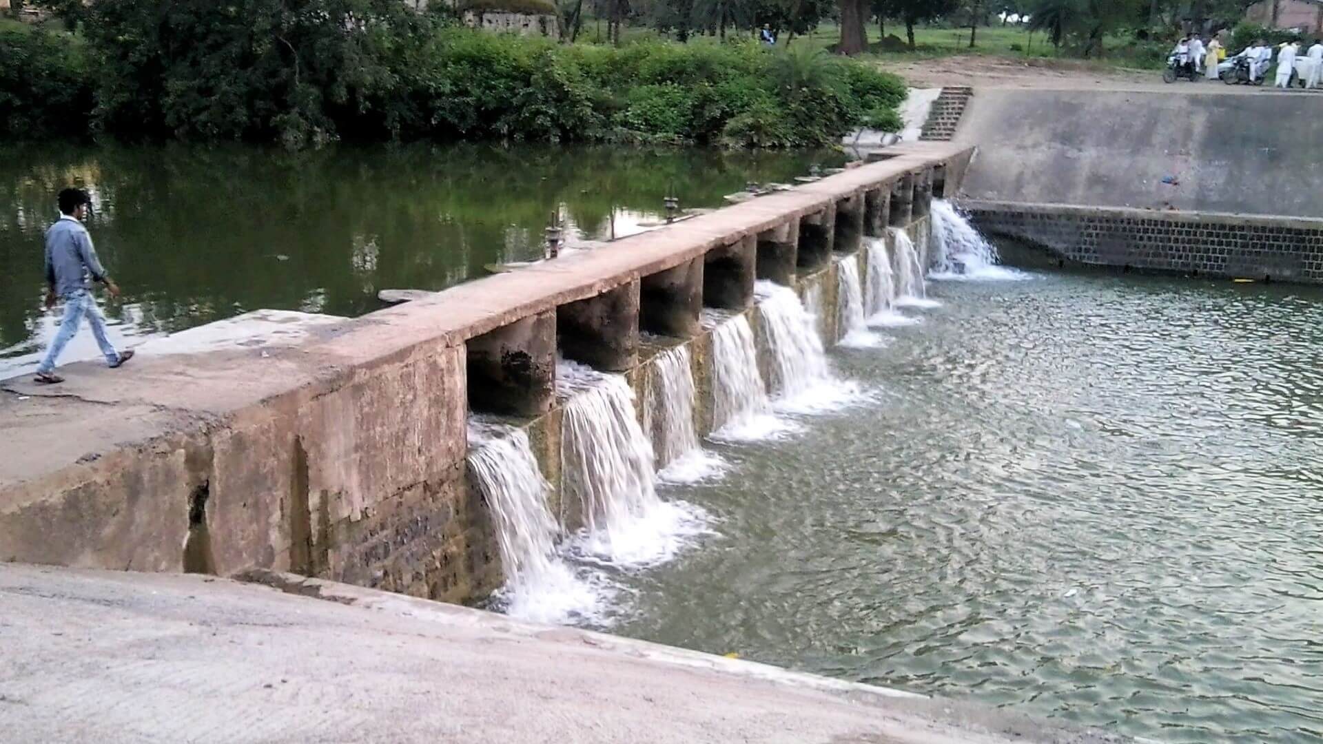 Man walking across small stone dam with water passing through a row of outlets