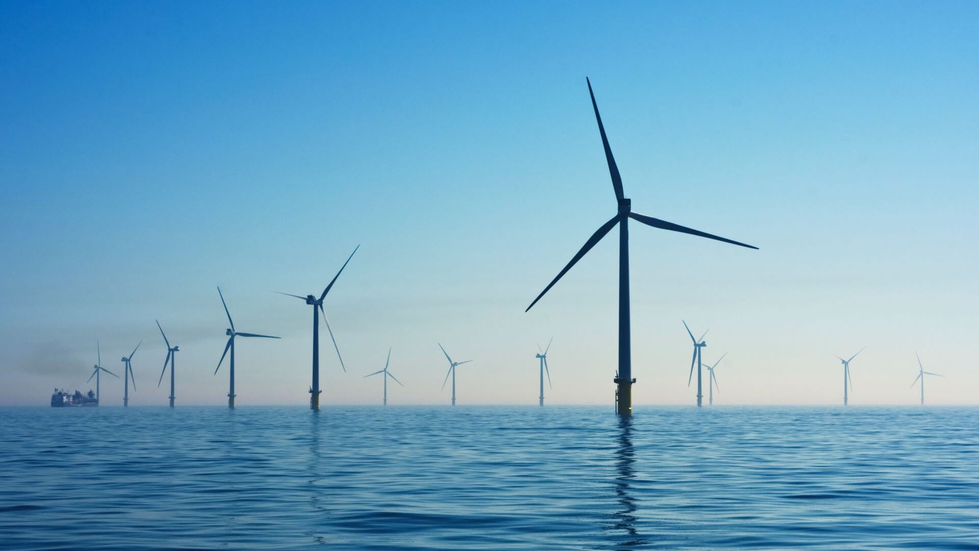 Rows of offshore wind farms in calm blue sea set against blue sky