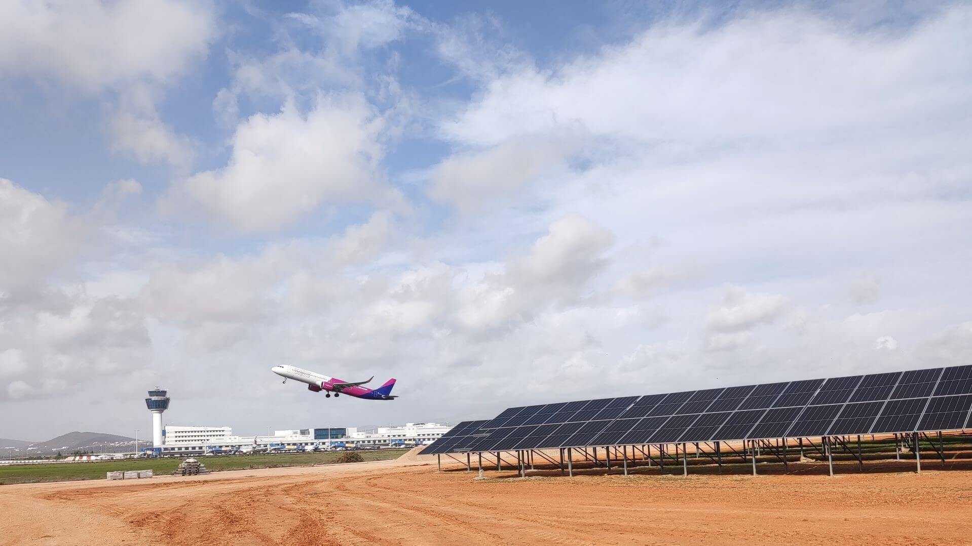 Rows of solar panels in foreground with distant view of airplane taking off 