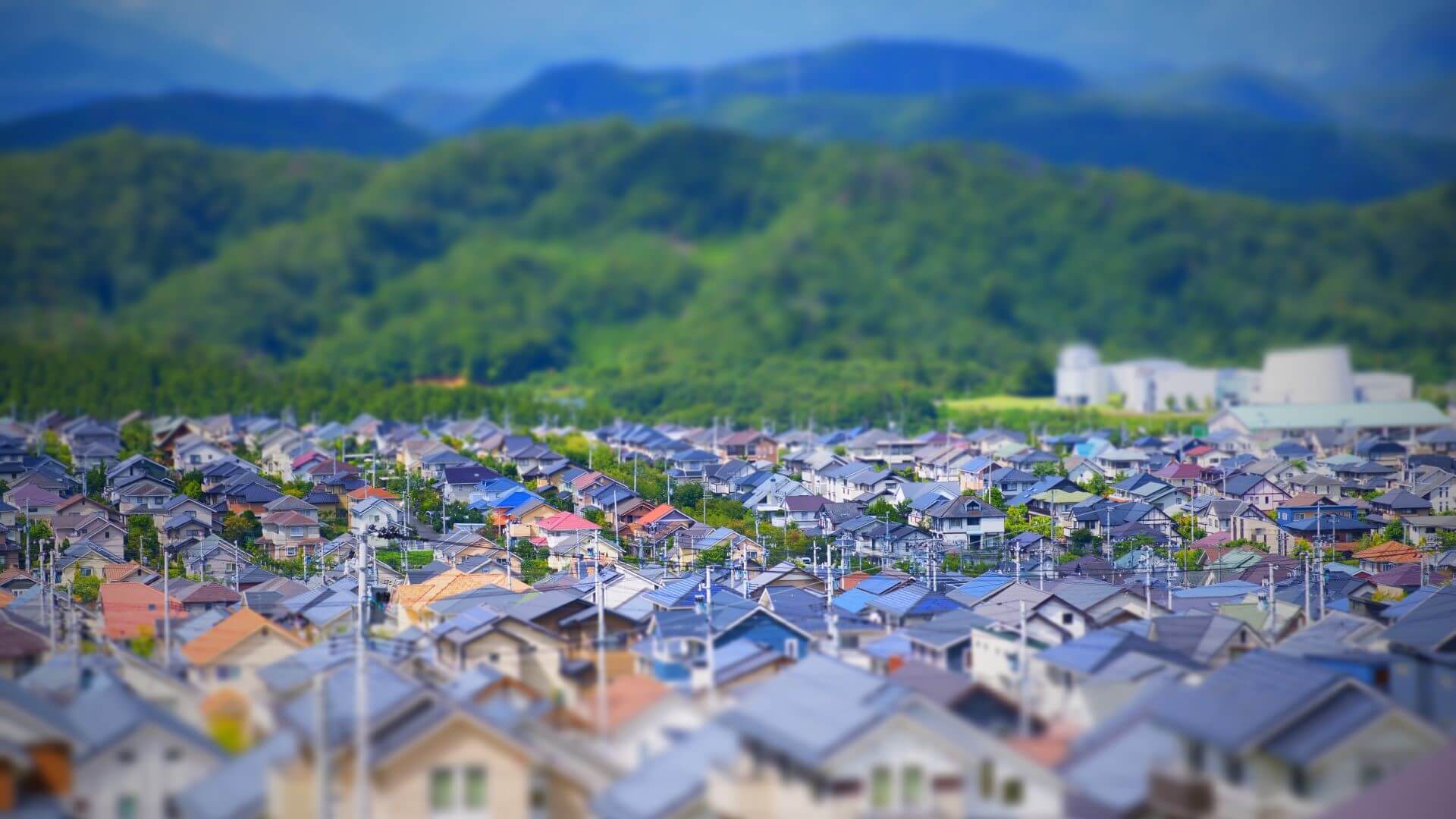 Row upon row of houses, with an industrial plant and mountains covered with trees in background