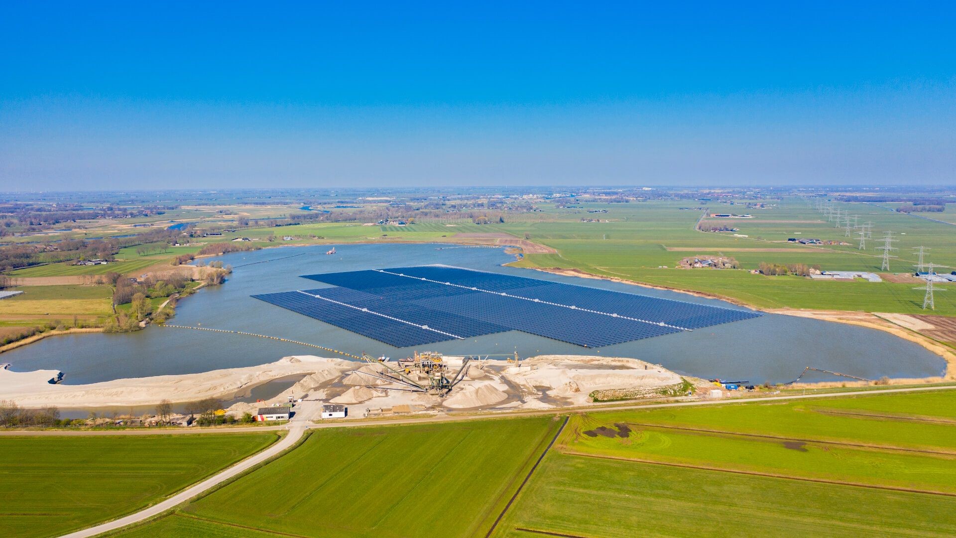 Floating solar panels on reservoir surrounded by green fields and a blue sky above