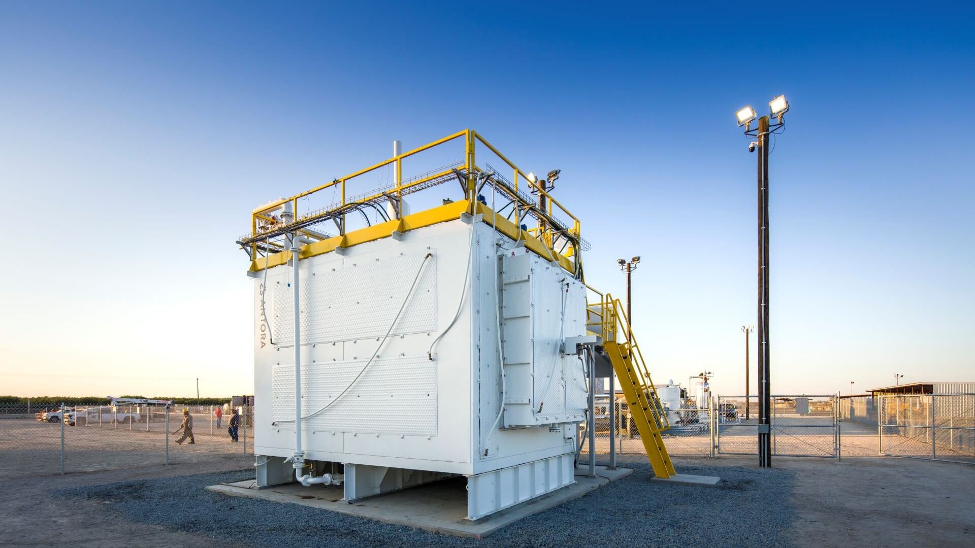 Large square storage battery next to floodlights with fenced off equipment behind