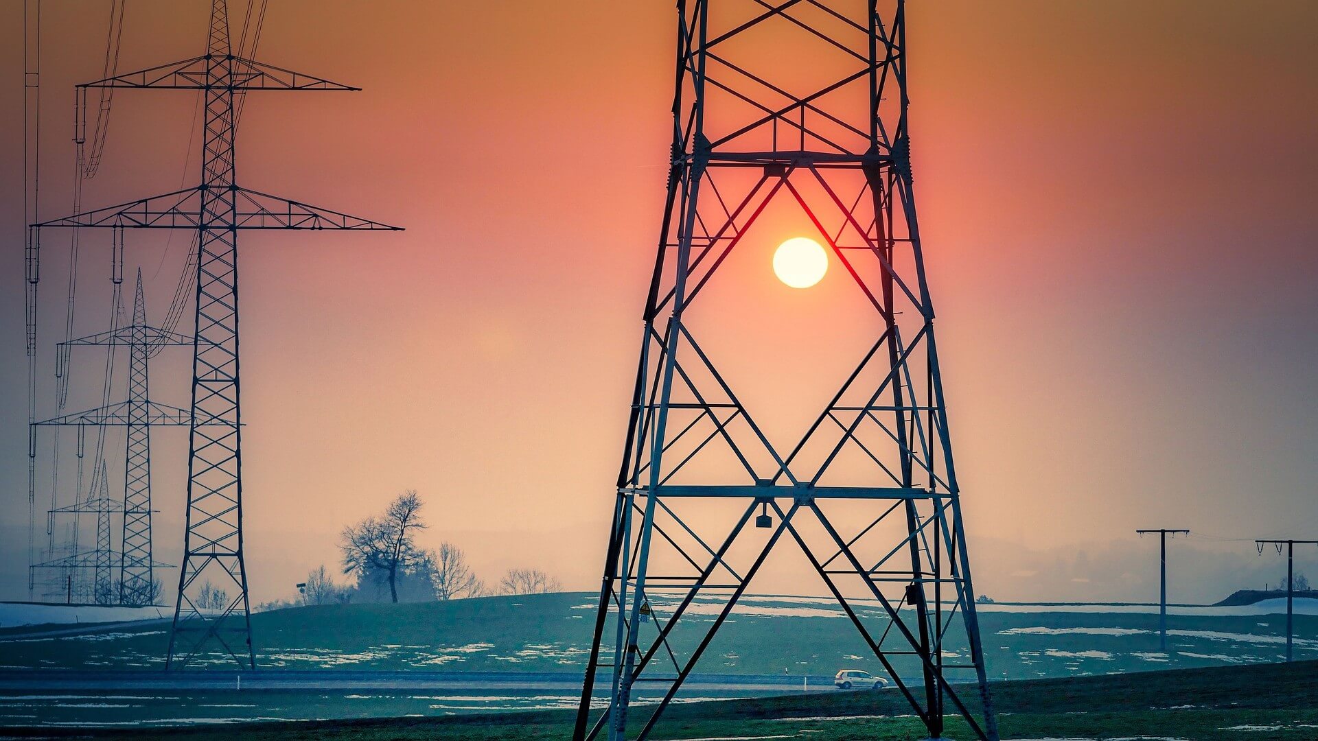 Silhouetted pylons and transmission lines set against orange sunset sky