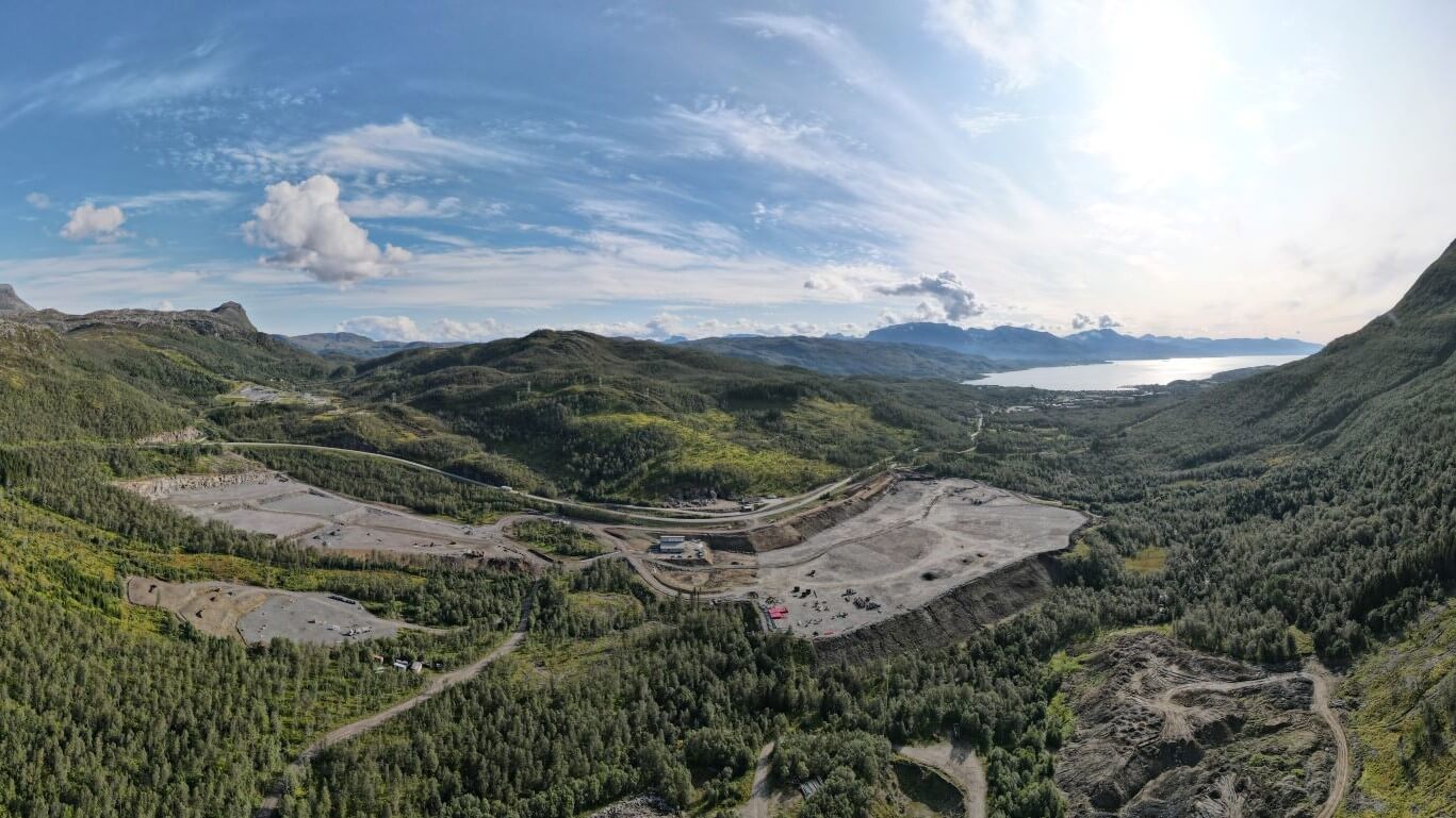 Aerial view over green hillsides with trees surrounding construction site, lake in background