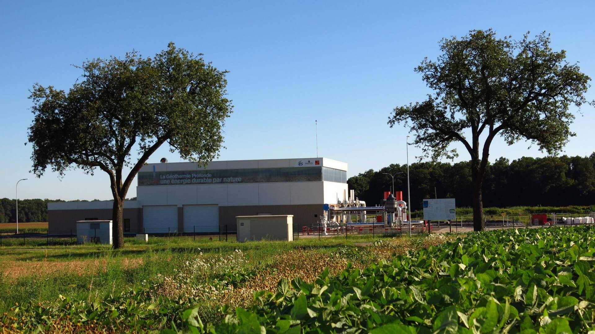 Outside photo of geothermal power plant, with green trees and hedge nearby