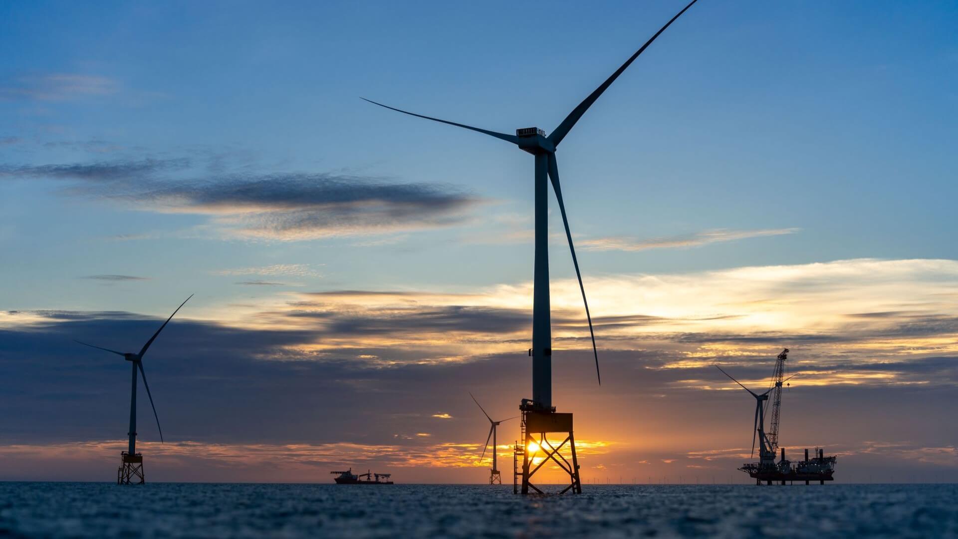 Four offshore wind turbines in calm sea silhouetted against sunset sky