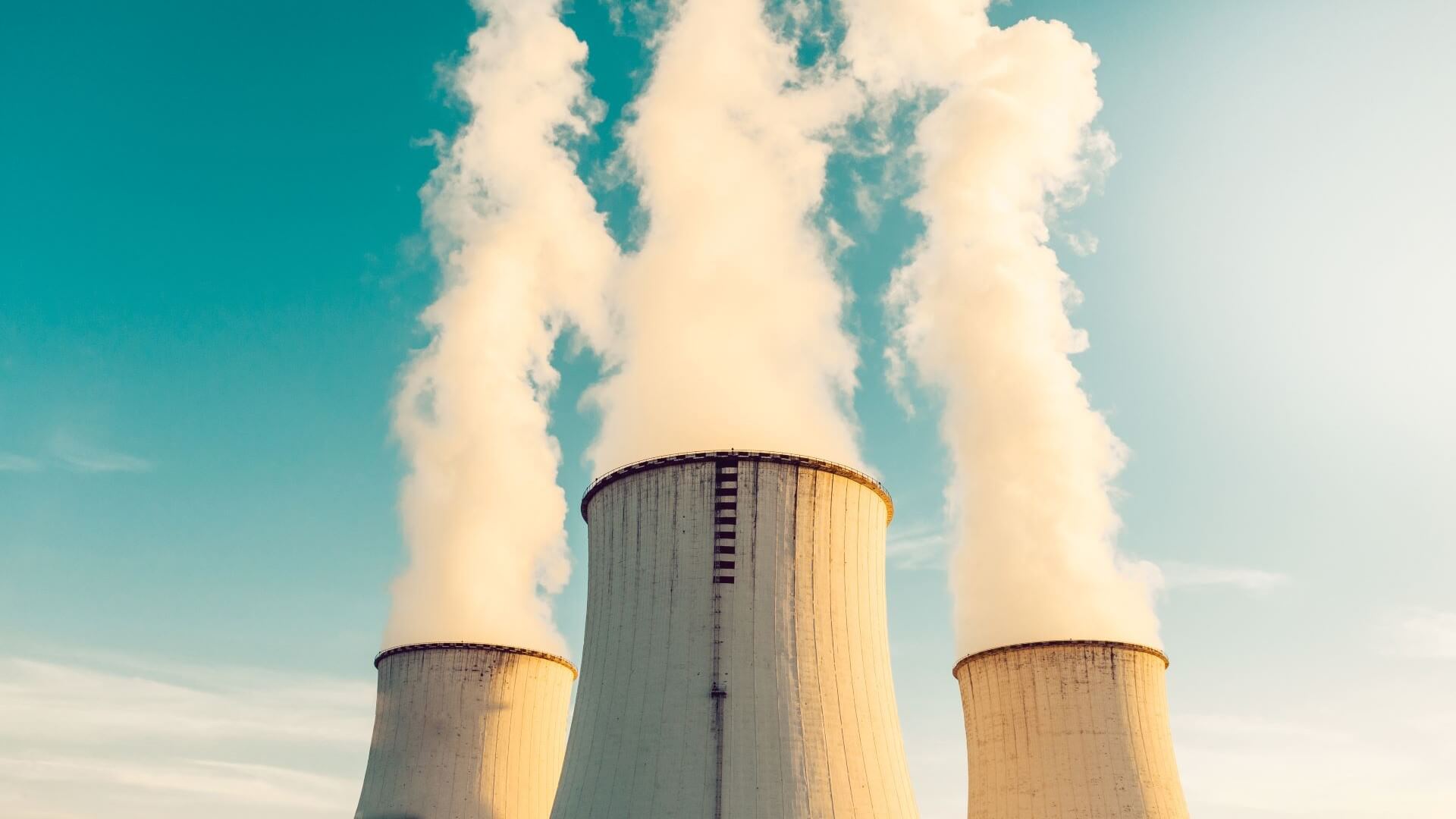 Three industrial chimneys with steam vapours billowing up into blue sky