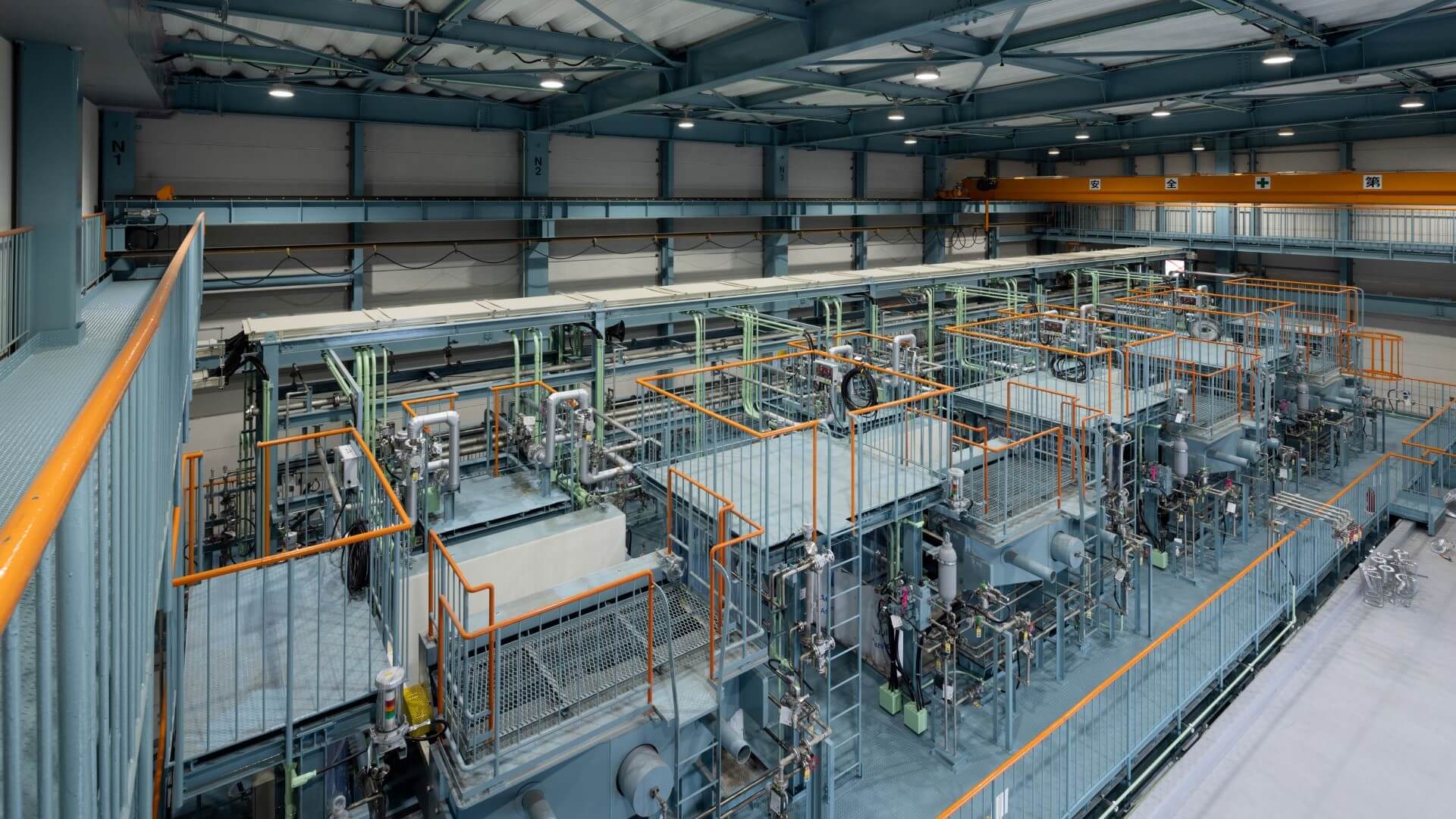 Inside warehouse type building looking over row of grey electrolyser units and pipework