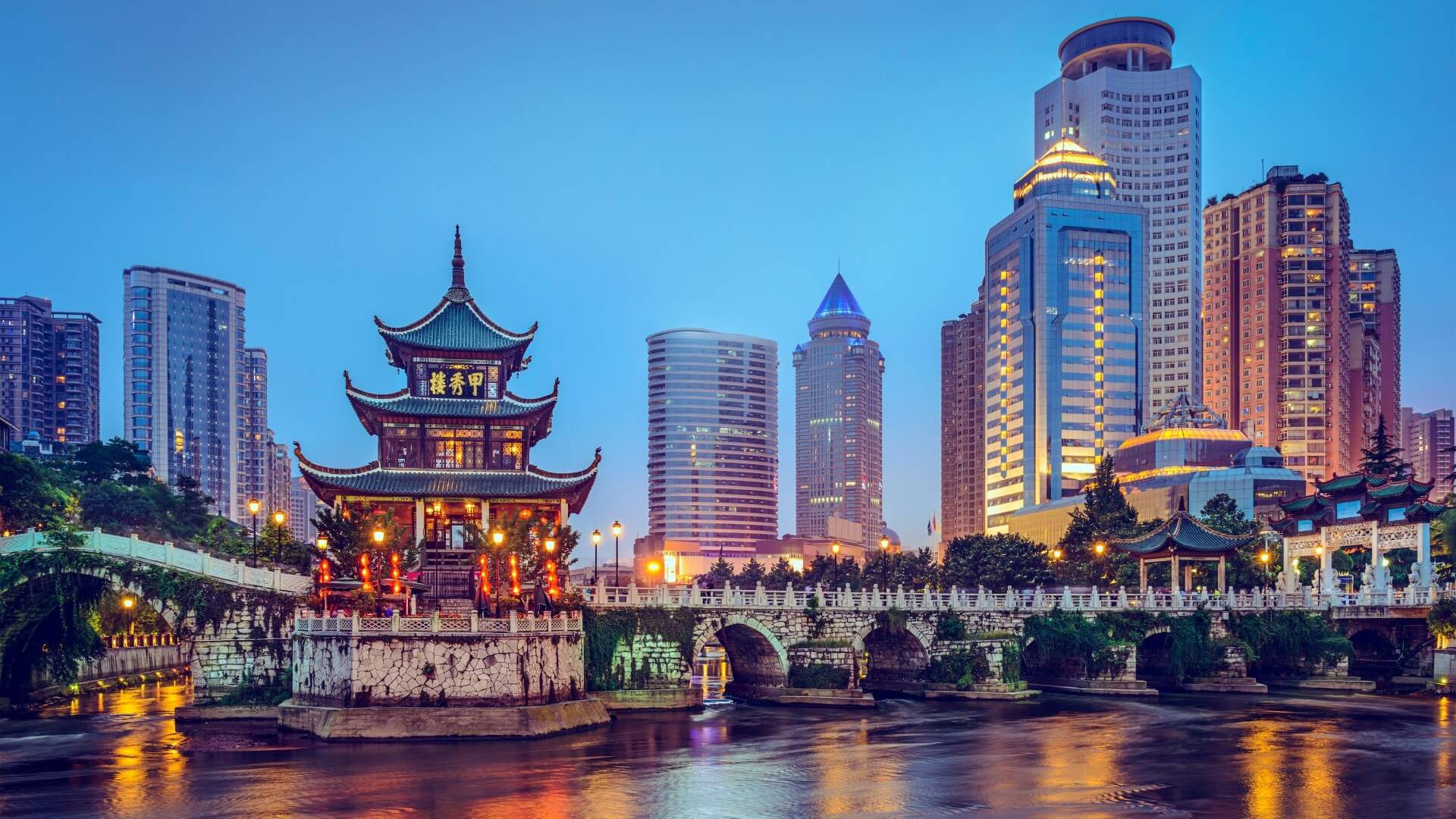 Elaborate Chinese sytle pagoda pavillion set in river in foreground, with modern cityscape behind