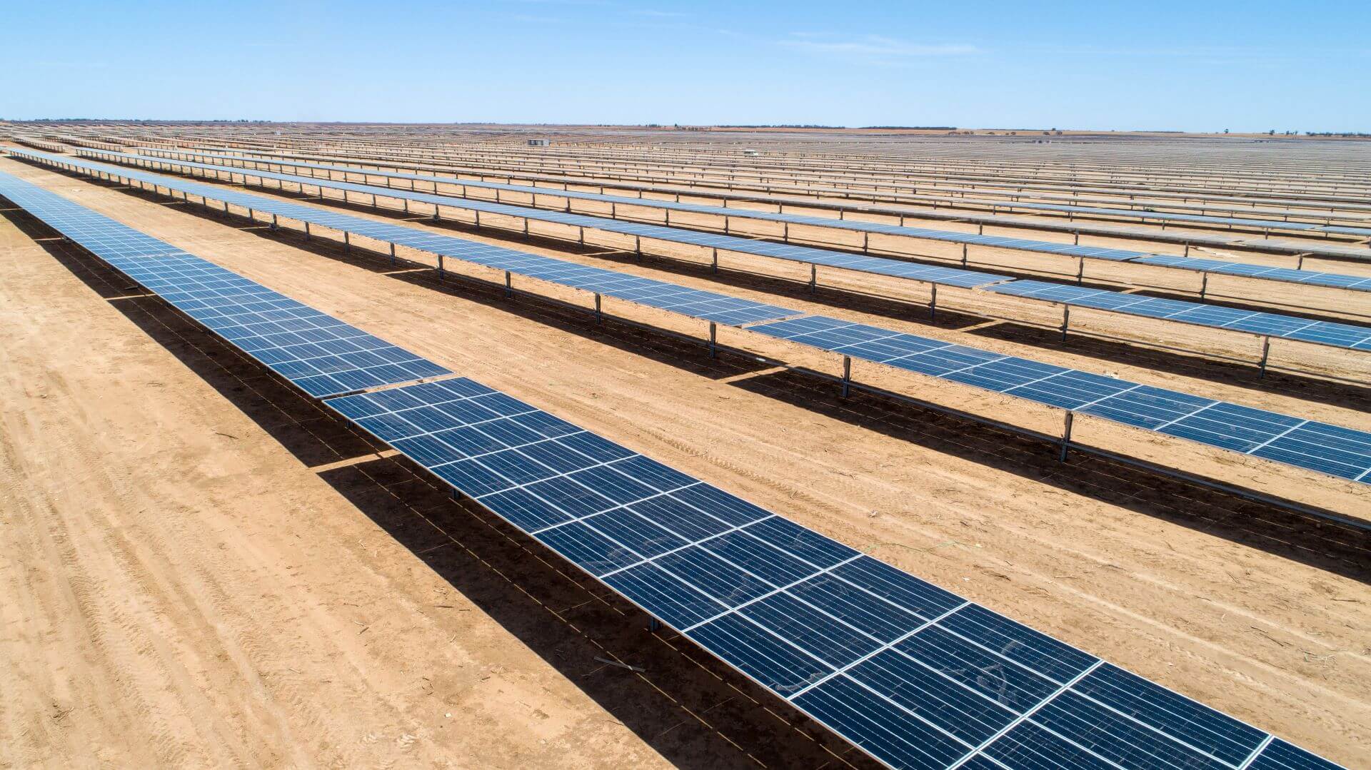 Rows of solar panels in dusty earth set against bright blue sky