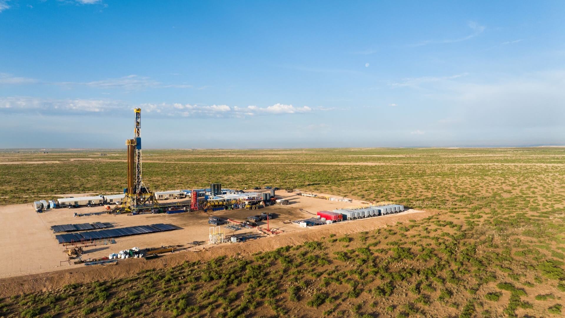 Aerial overview of unconventional drilling operations in flat, scrubby landscape