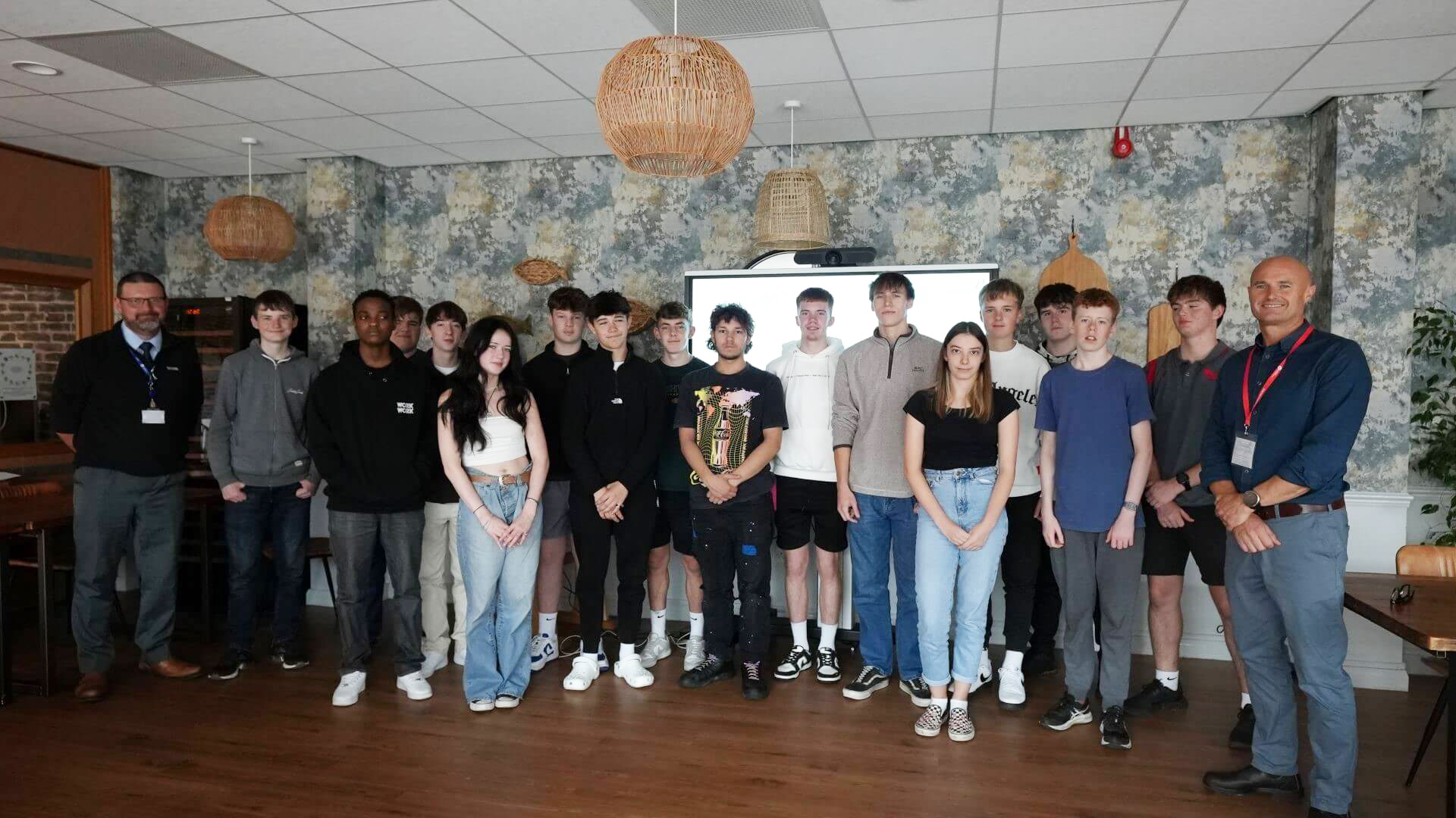 Rows of young students standing in front of big screen with trainer standing to left of them