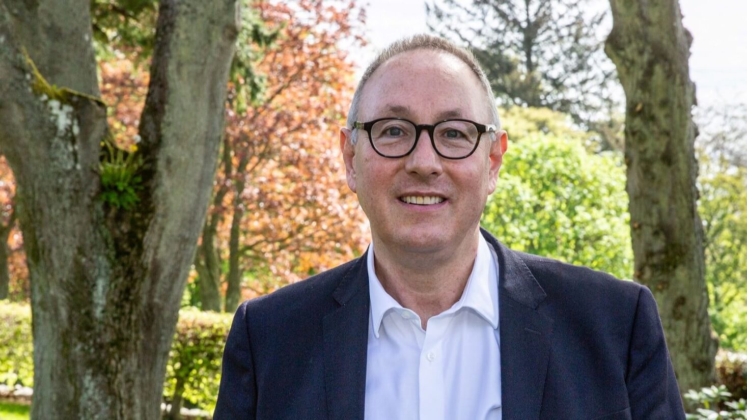 Head and shoulders photo of Professor Paul de Leeuw,, with trees and grass behind him