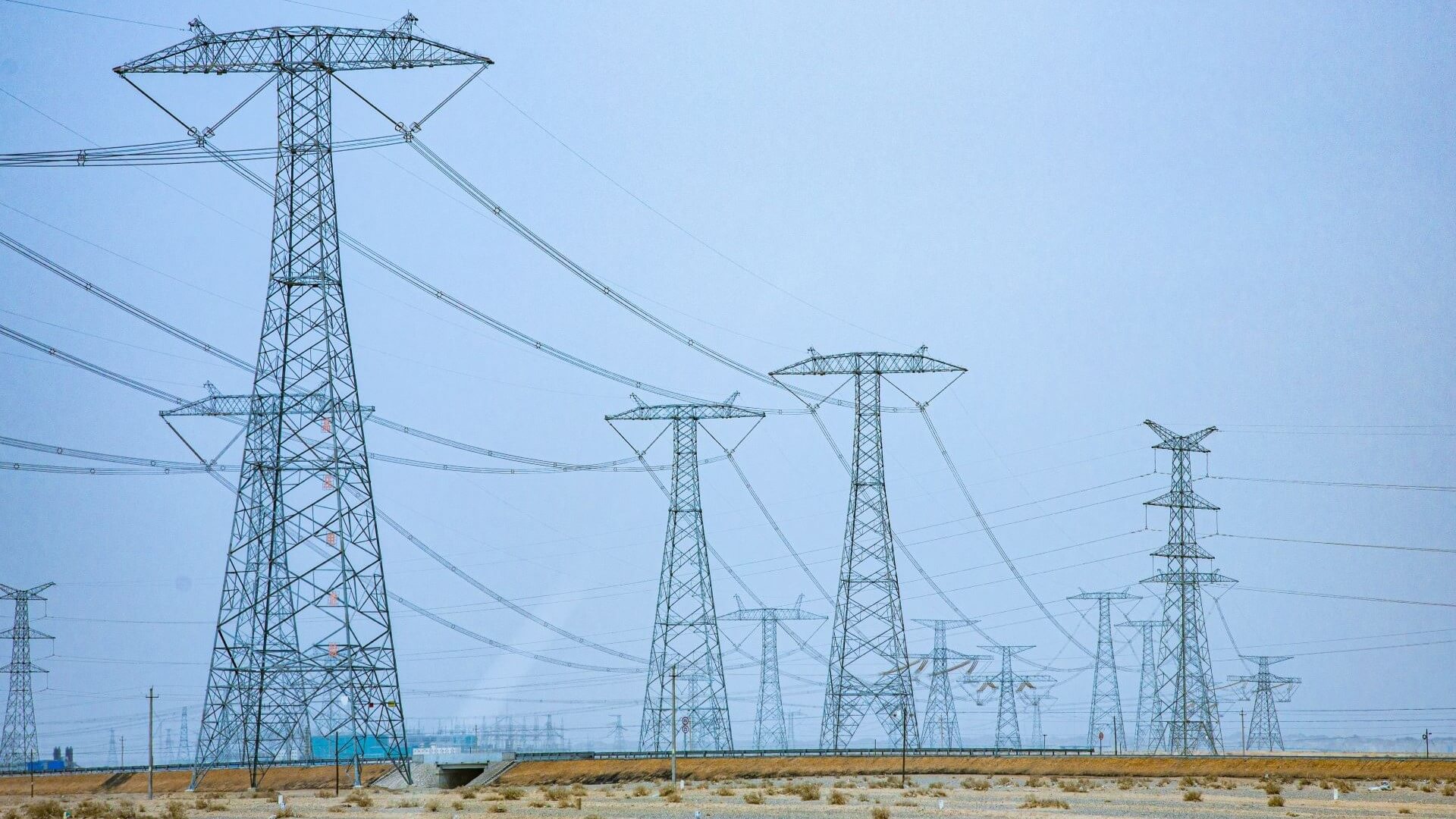 Rows of electricity pylons and transmission lines extending into the distance, set against a blue sky