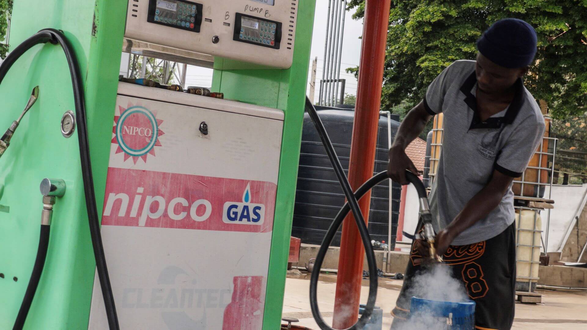 Man standing next to fuel pump, holding pump nozzle and filling a gas cylinder with LPG