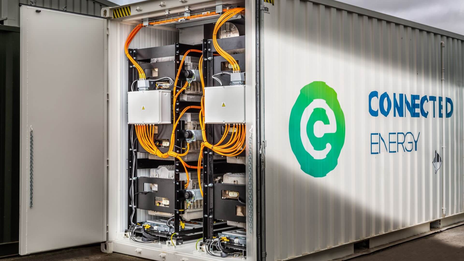 Shipping container with door open showing electric charging equipment and cabling inside