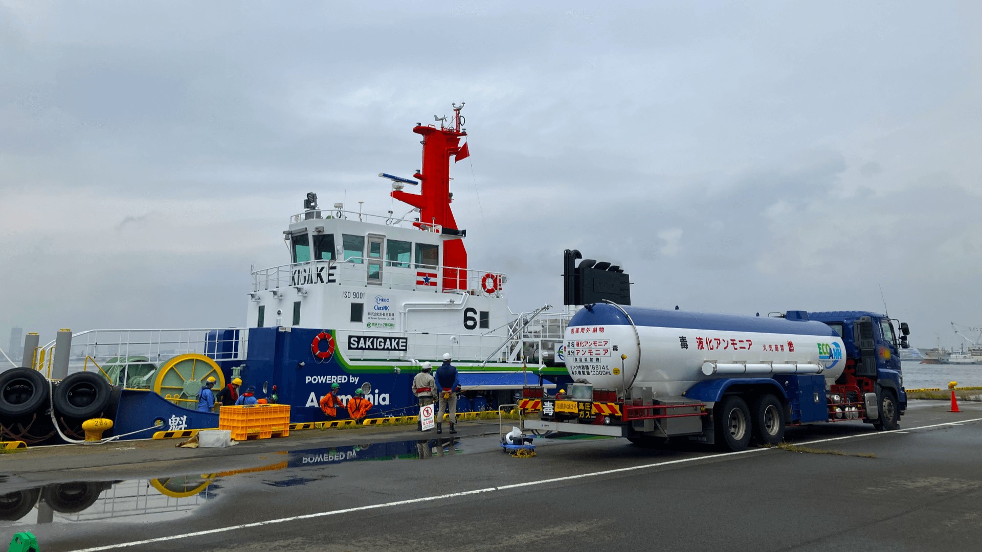 Small tug vessel moored alongside jetty, being fuelled up by a road tanker