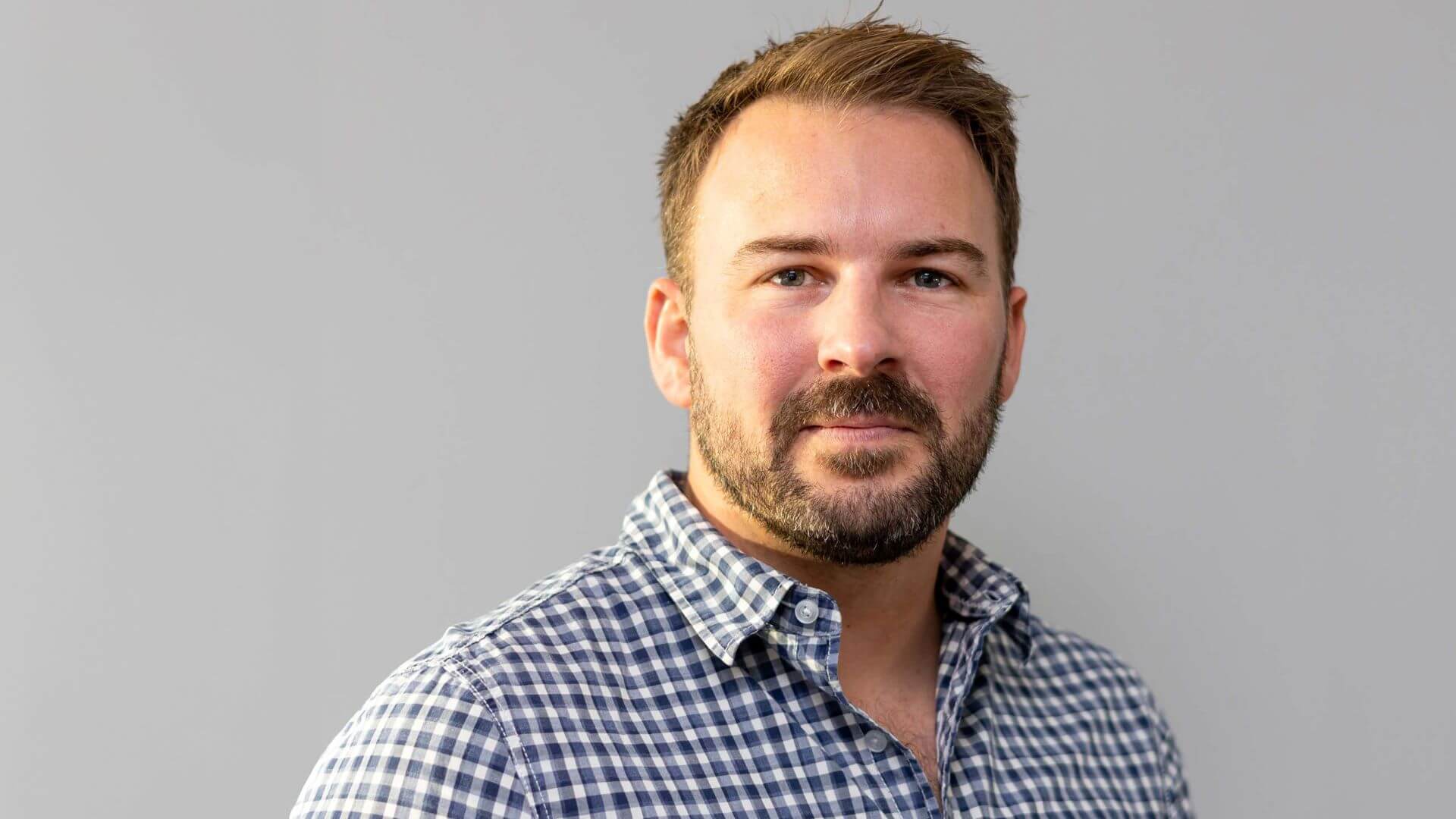 Head and shoulders photo of man with grey blue background behind