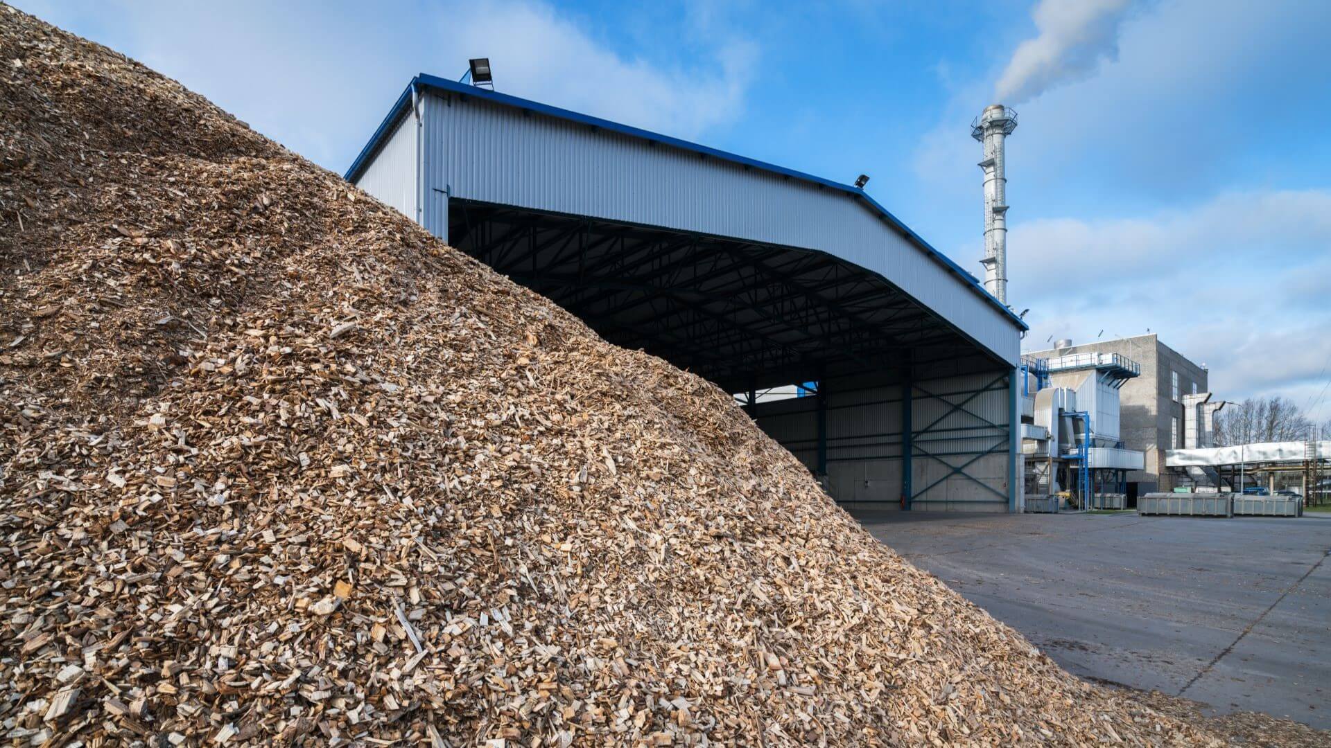 Large pile of woodchips in foreground of pic, with industrial plant building in background