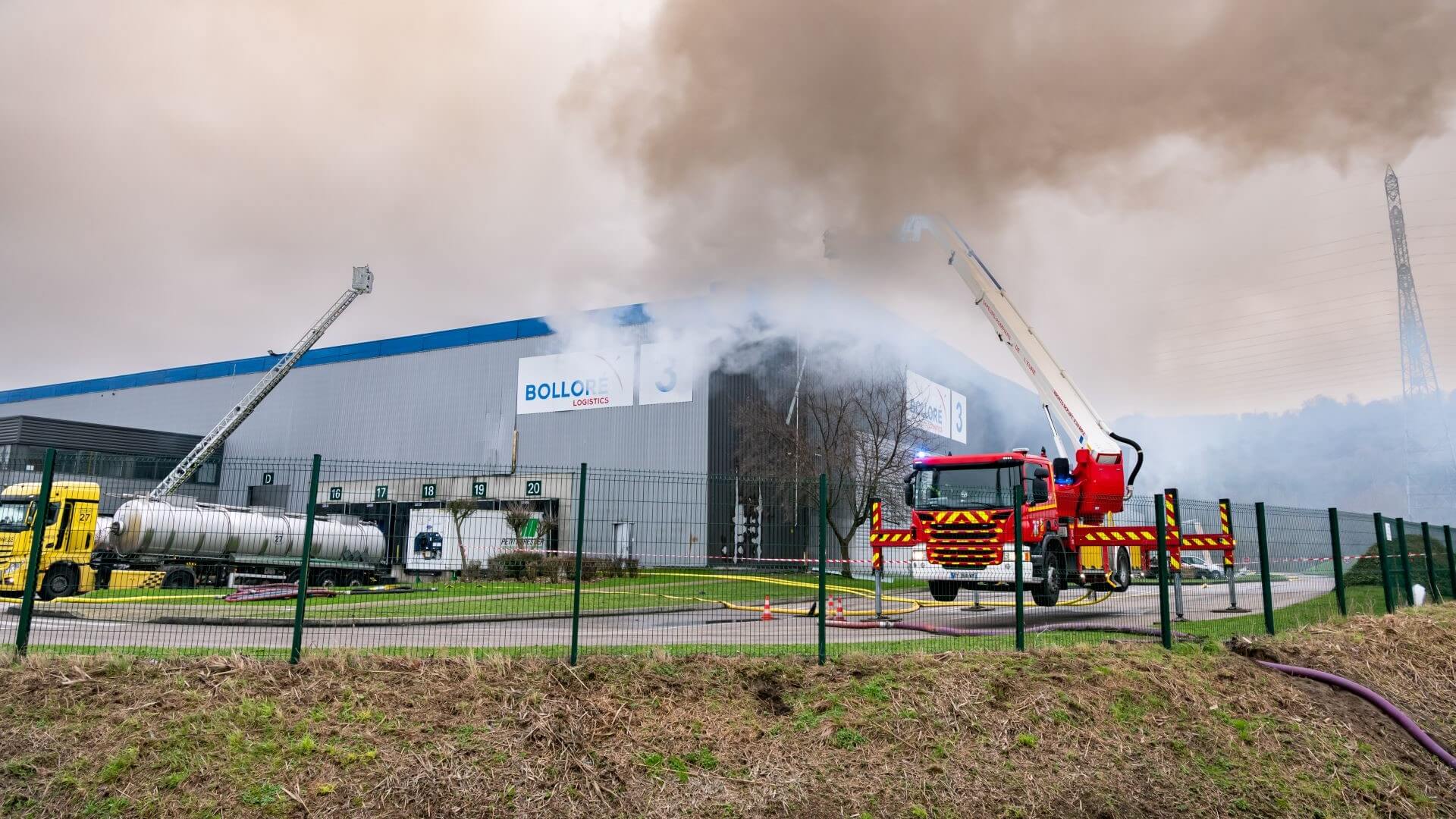 Fire engine outside a warehouse that is on fire with billowing smoke rising in the air