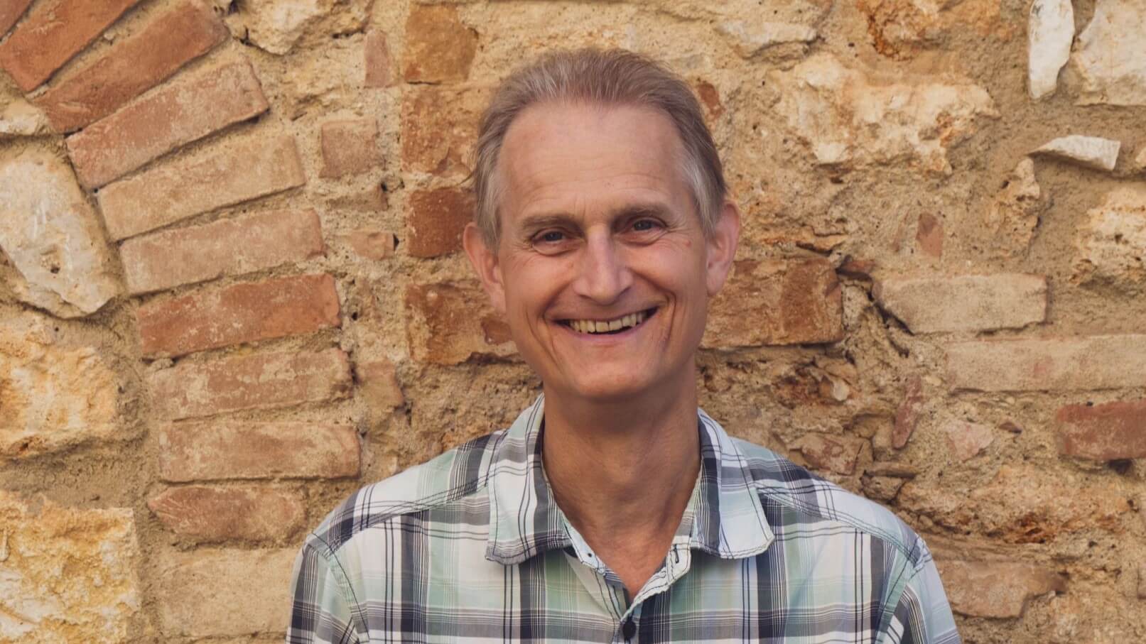 Head and shoulders photo of Tim Lines with sandy coloured, old brick wall behind