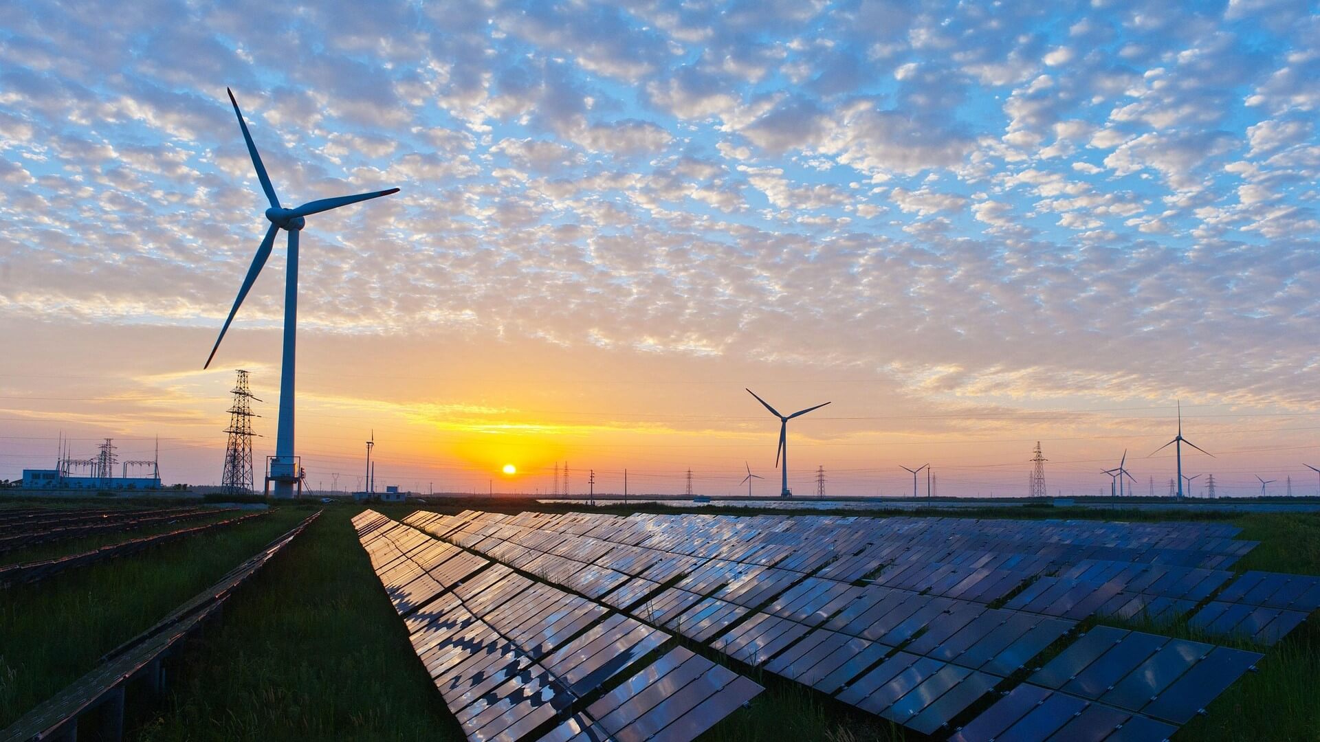 Wind turbines and solar panels at sunset