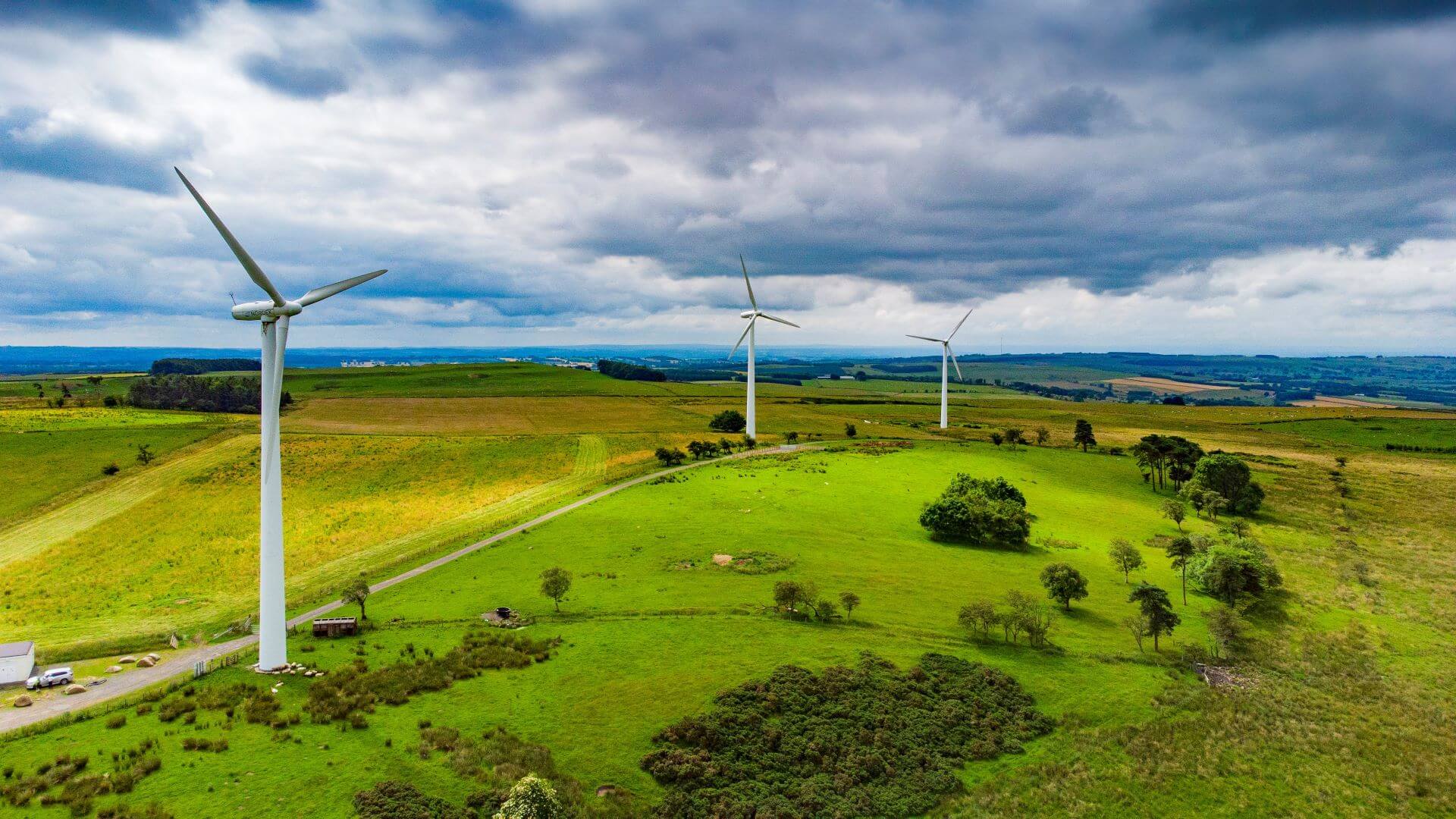 Aerial view of 3 onshore wind turbines set in green countryside with blue sky and white clouds