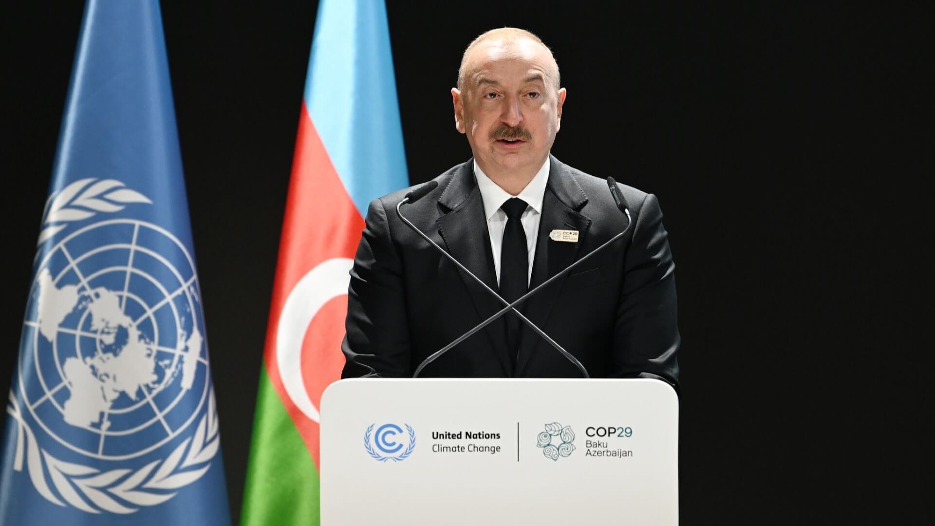 Azeri President Ilham Aliyev standing at lecturn with Azeri and UN flags behind him