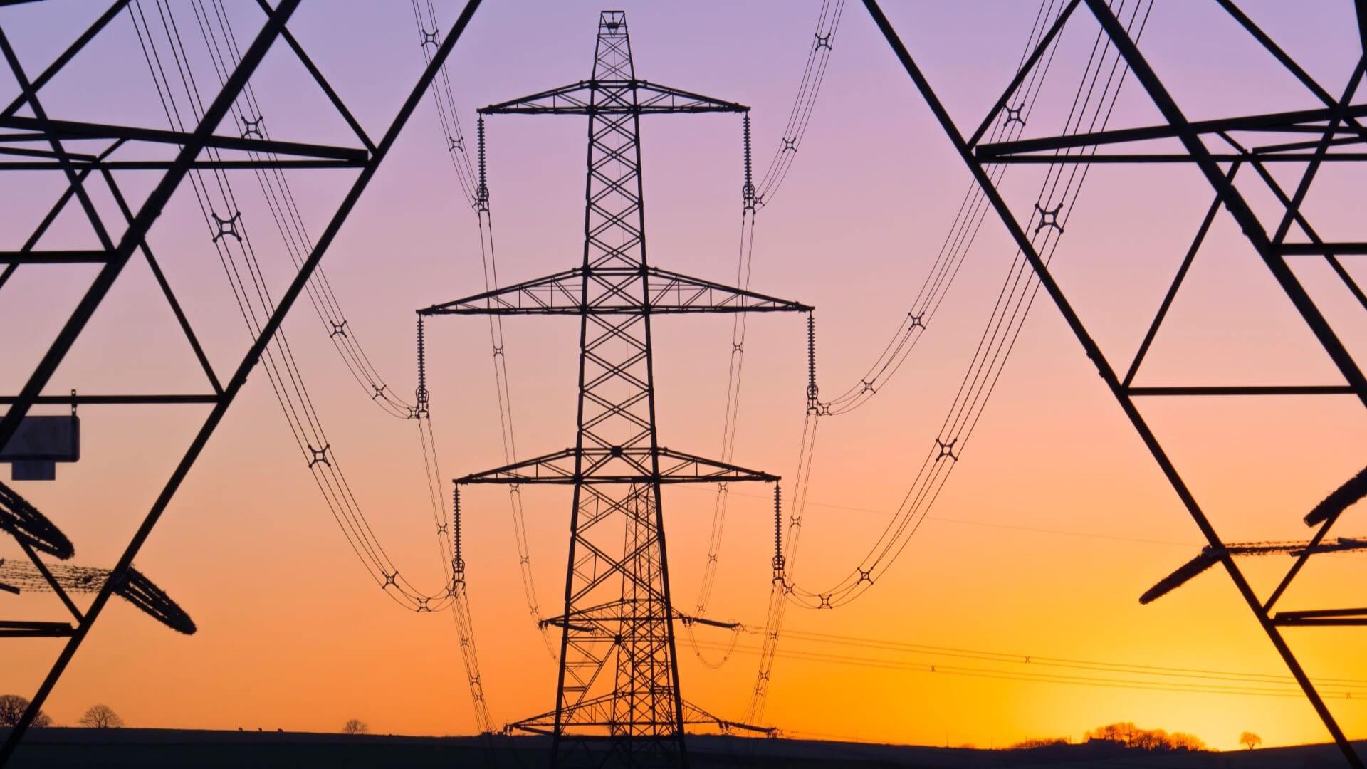 Electricity pylons silhouetted against sunset sky