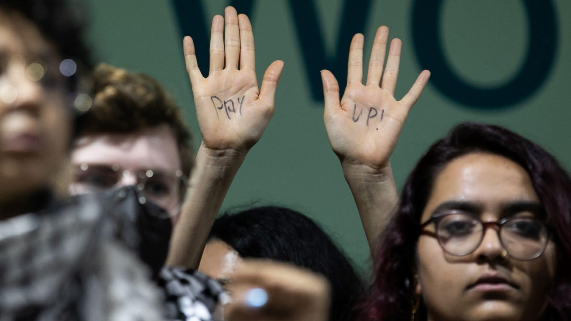 Close up of protester's raised hands with 'Pay' and 'Up' written on palms of hands