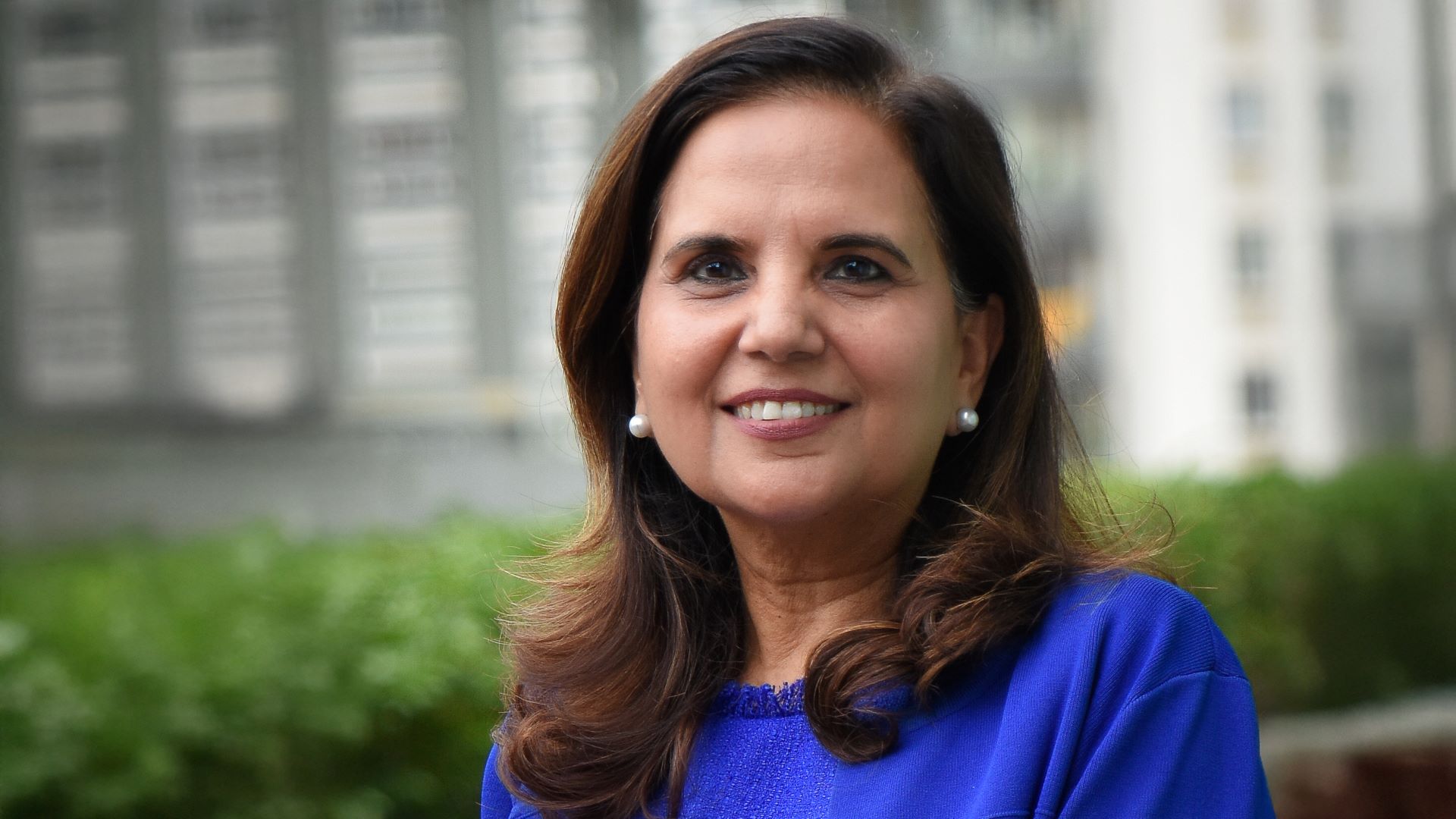 Head and shoulders photo of Kavita Gandhi in front of blurred building and hedge