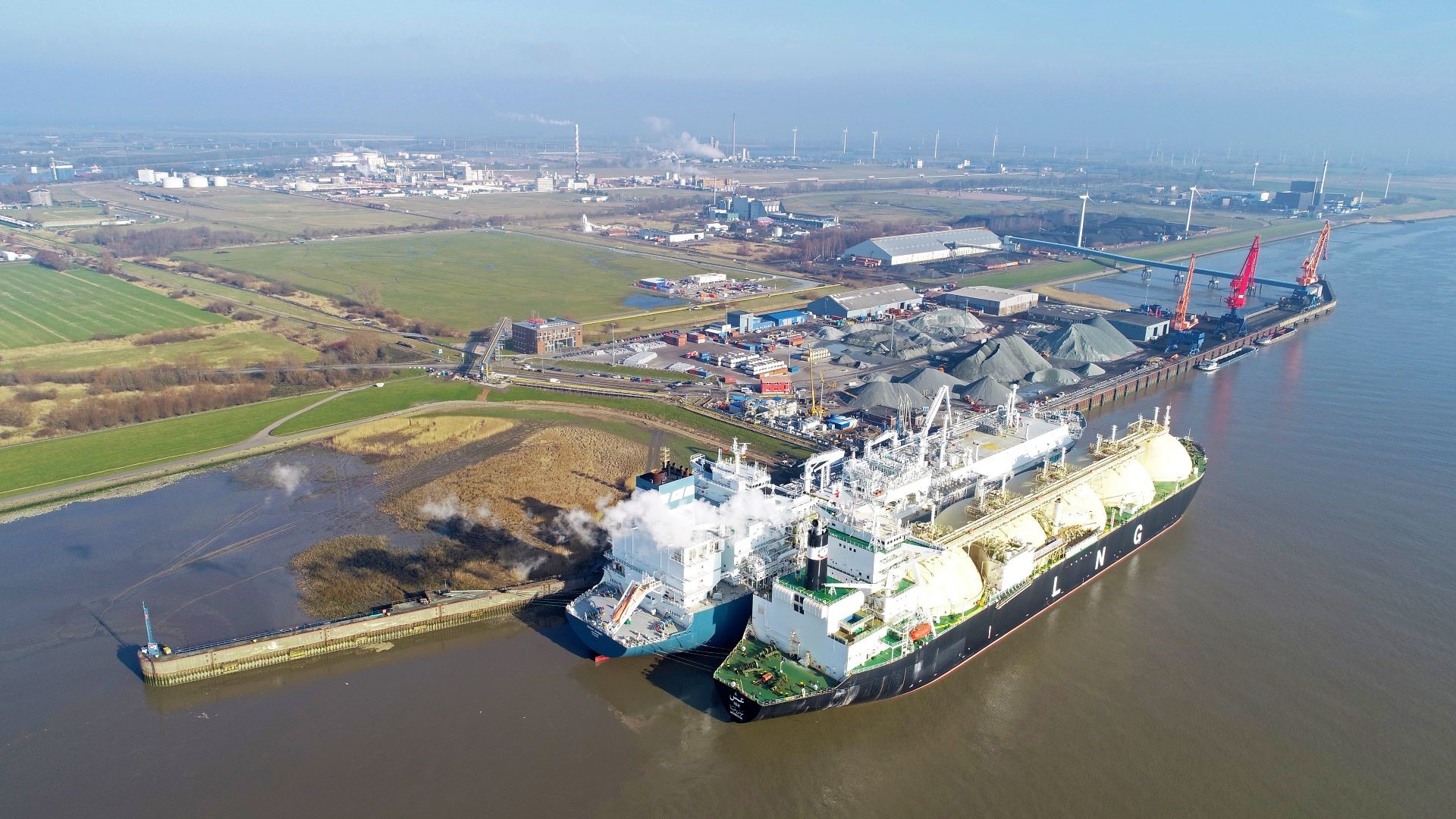 Aerial view over LNG tanker moored at port jetty and unloading cargo