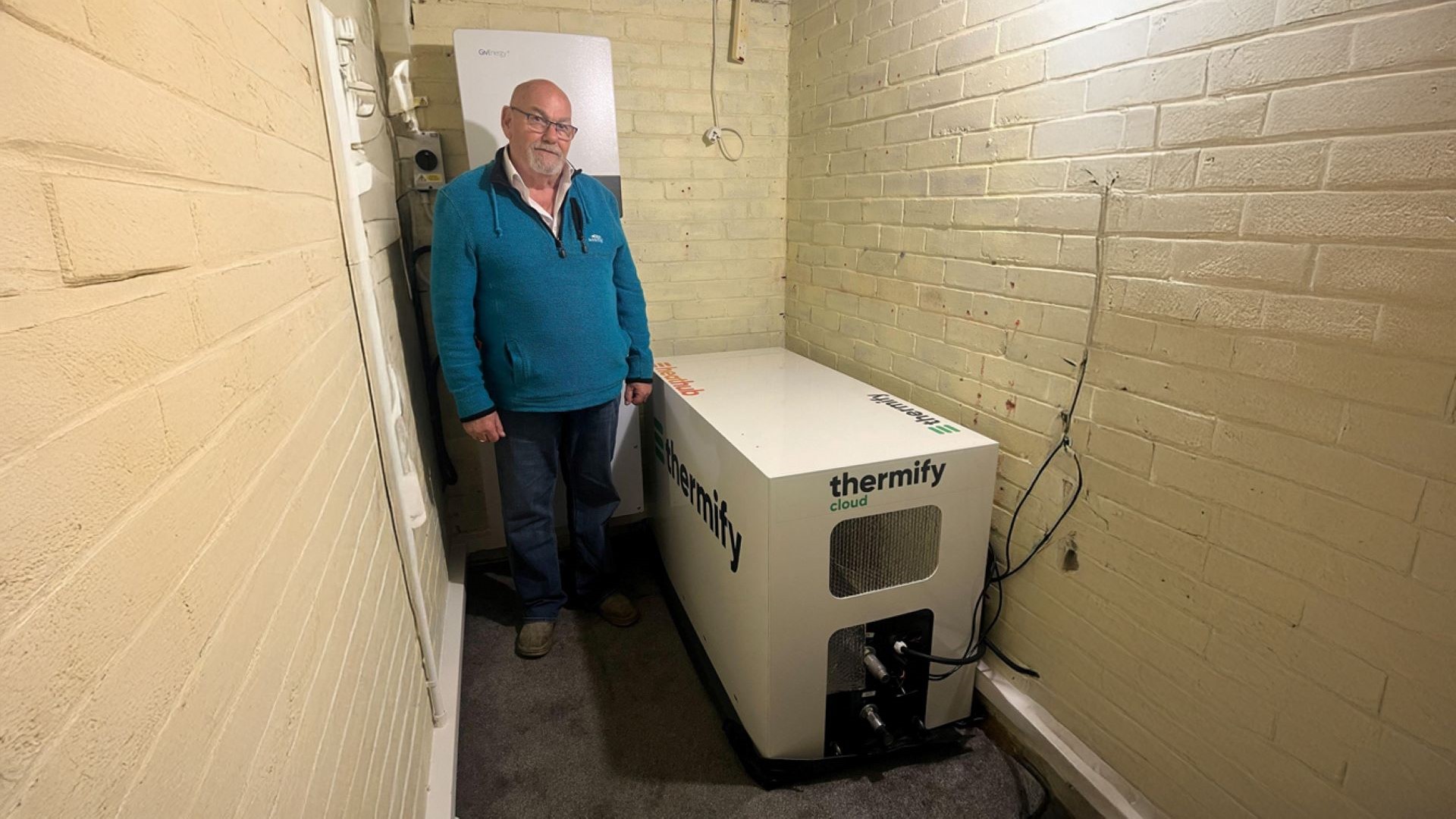 Man standing next to heat unit in brick outbuilding