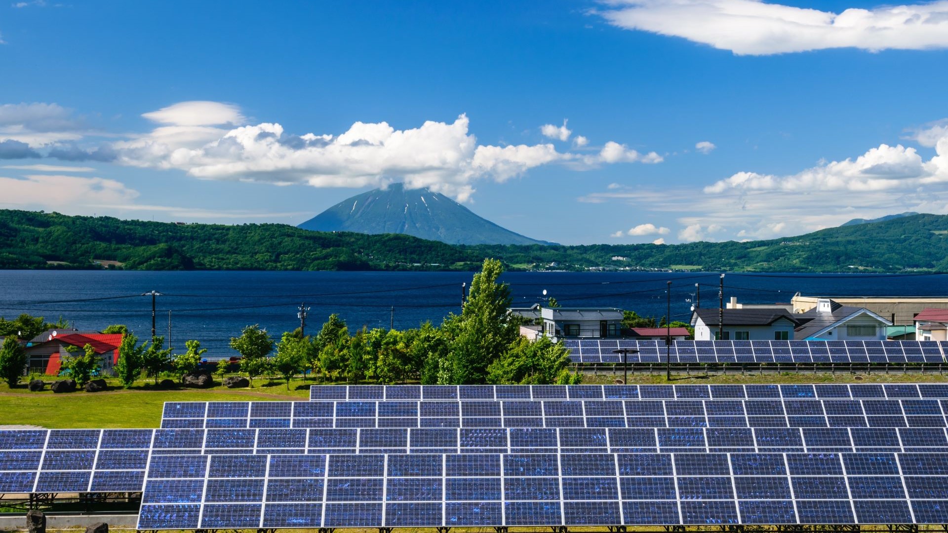 Rows of solar panels in foreground, mountain and lake in background