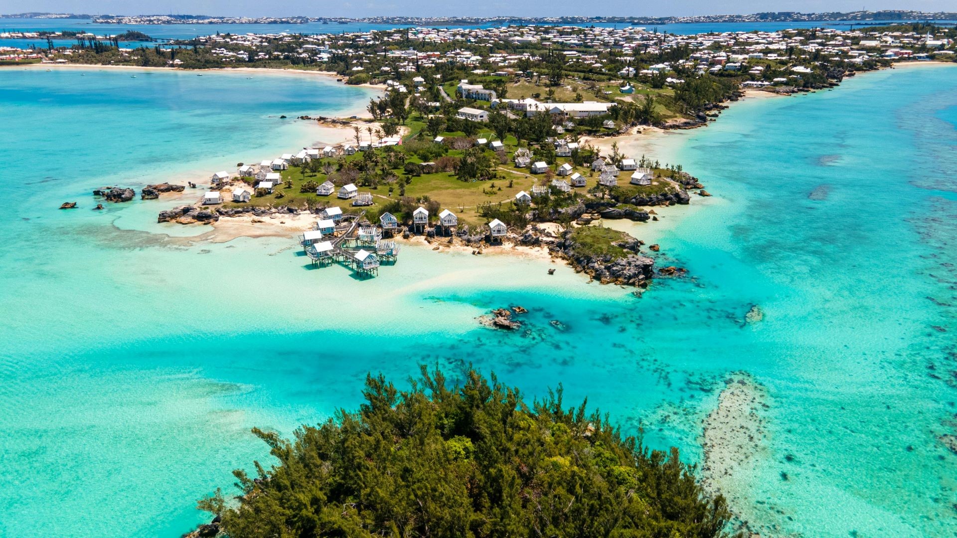 Aerial view over tropical island with green trees and small residential buildings, with golden sands and surrounded by green blue sea