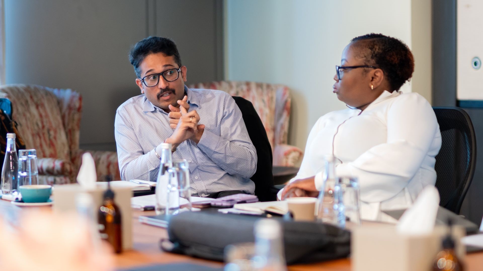 Image of man sitting at business meeting table, talking to woman sat to the left of the picture