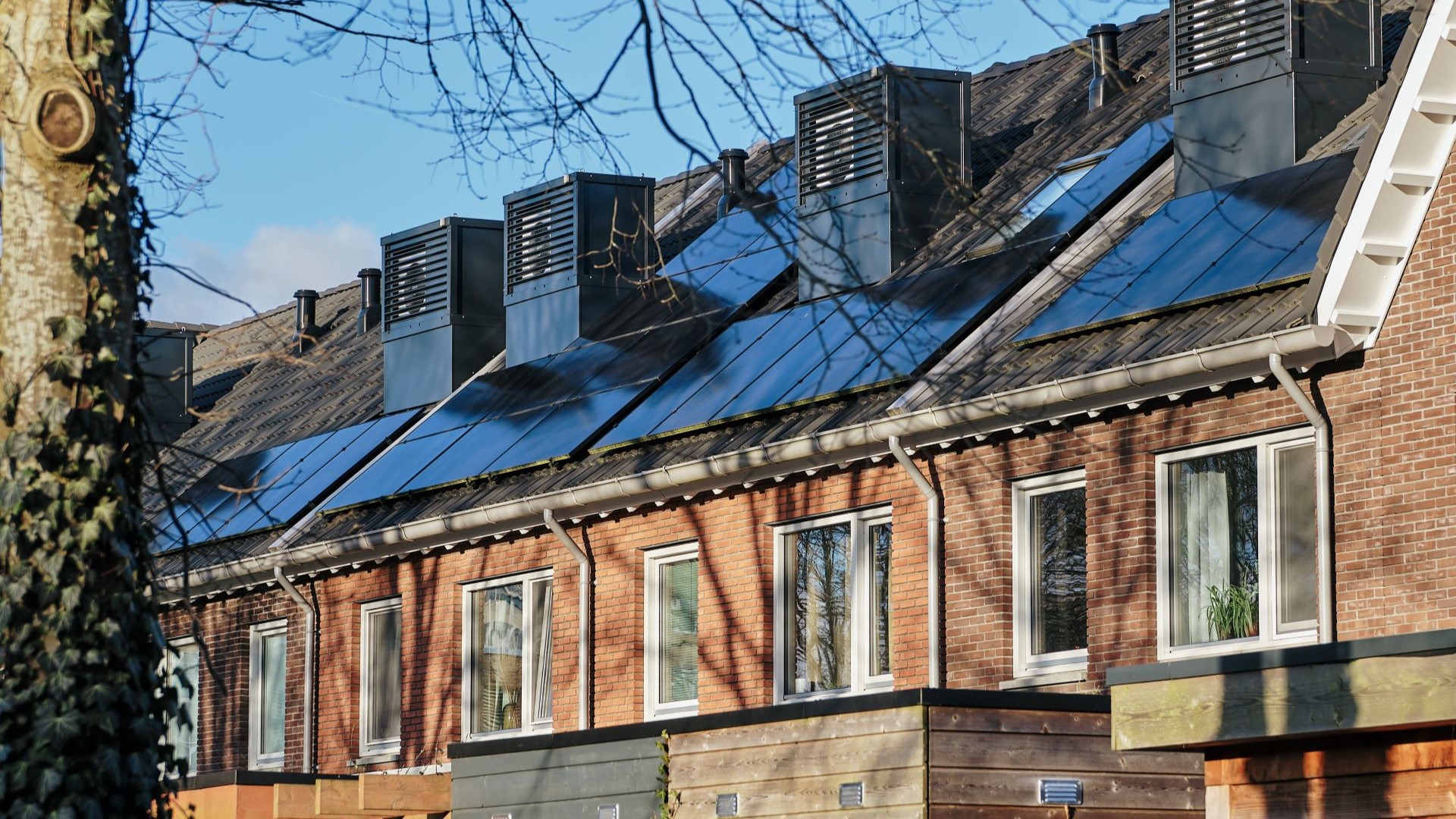 Row of modern terraced housing with rectangular heat pumps installed alongside solar panels on roofs